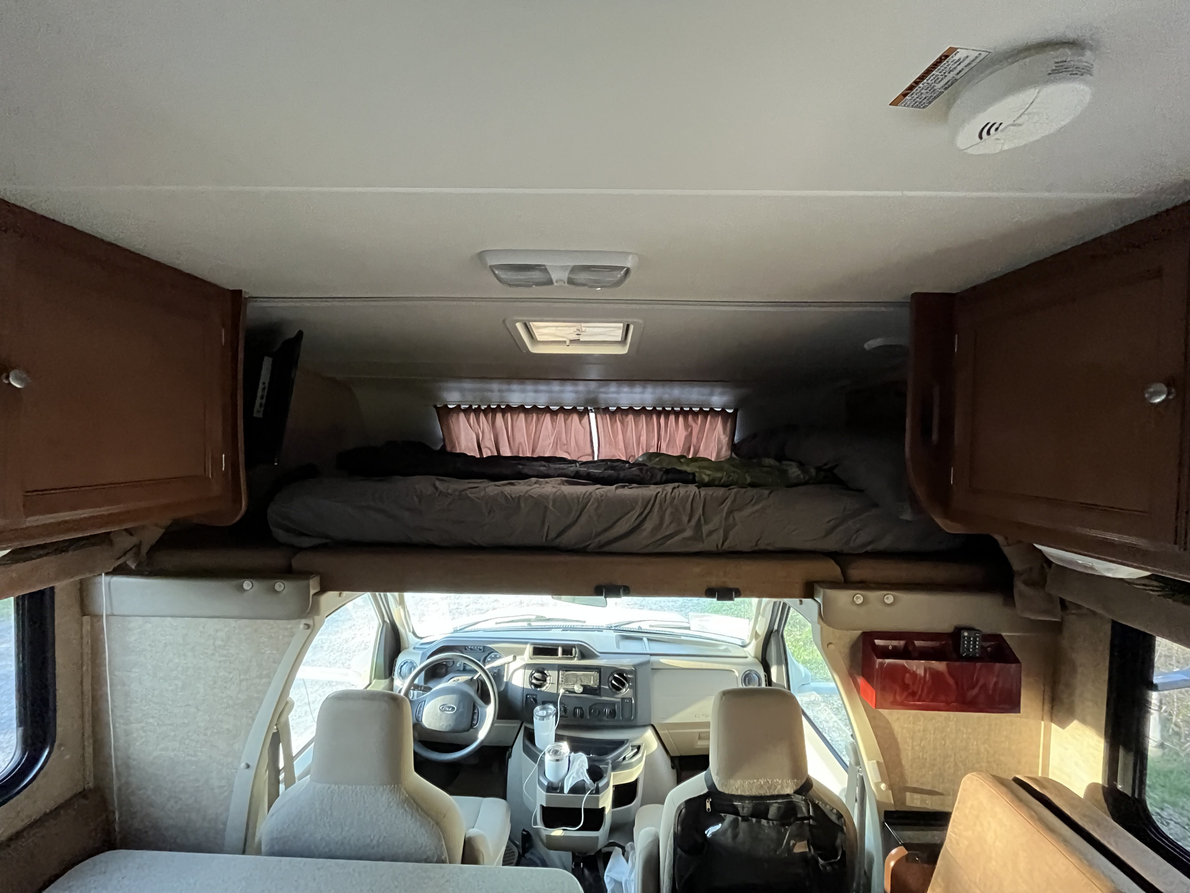 Inside an RV rental motorhome, showing the front cab area, seats, and overhead bed.. Coachmen Leprechaun 2014