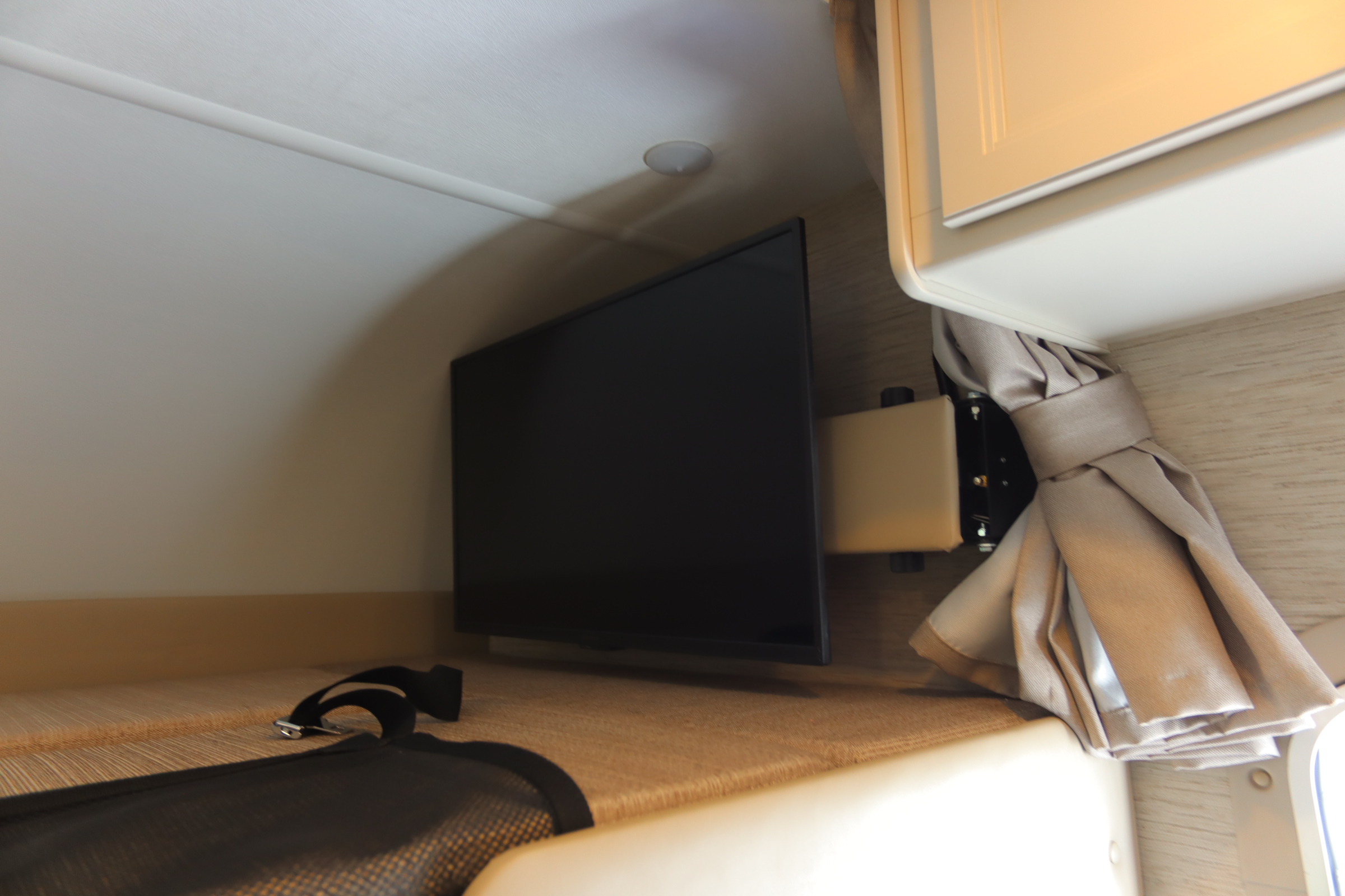 RV rental interior: mounted TV, overhead light, curtain, cabinet, and bunk bed with seatbelt. Ideal for travel.. Thor Motor Coach Chateau 2024