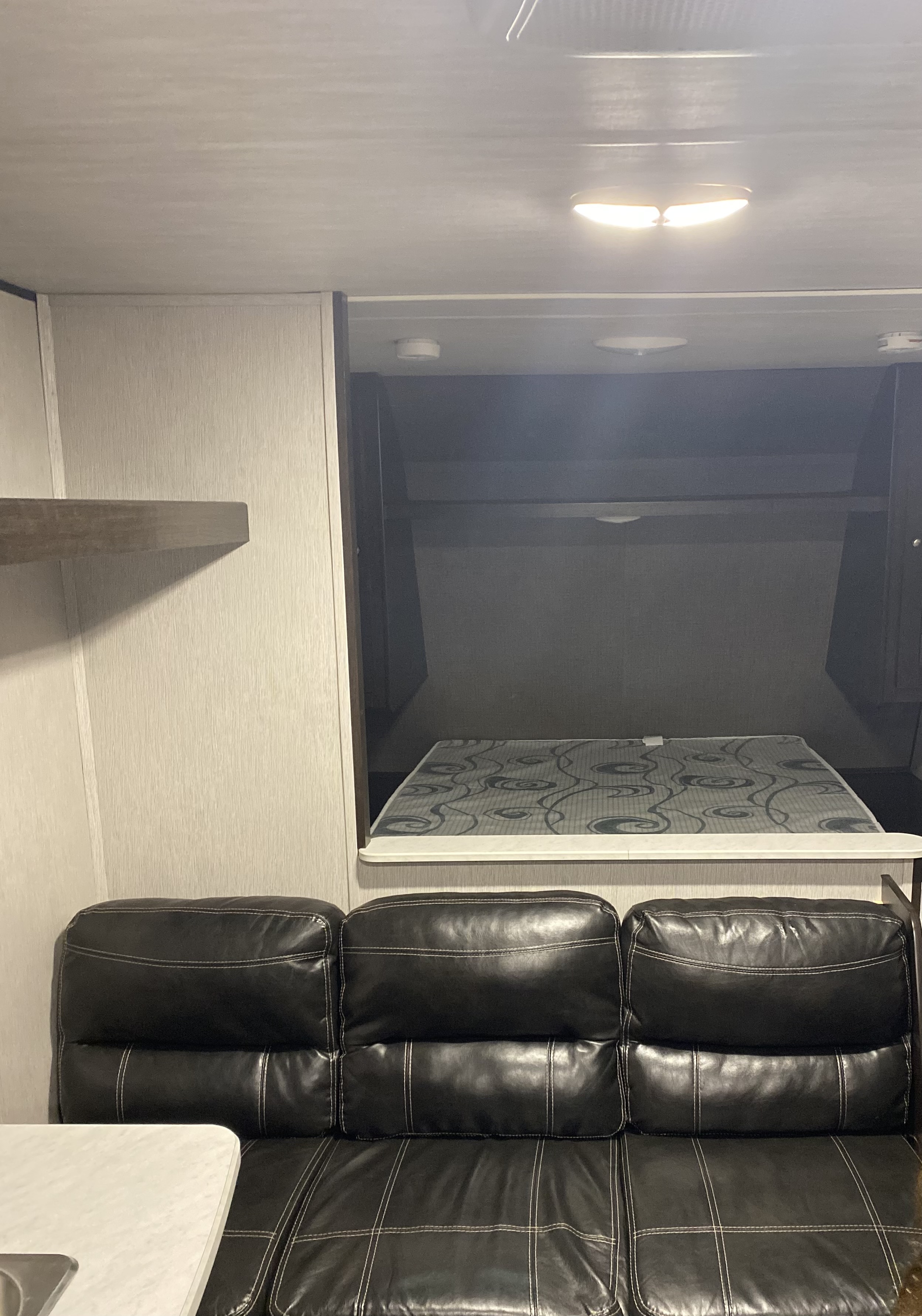 RV rental interior features a comfy black leather sofa below a neatly integrated loft bed.. Heartland RVs Prowler 2021