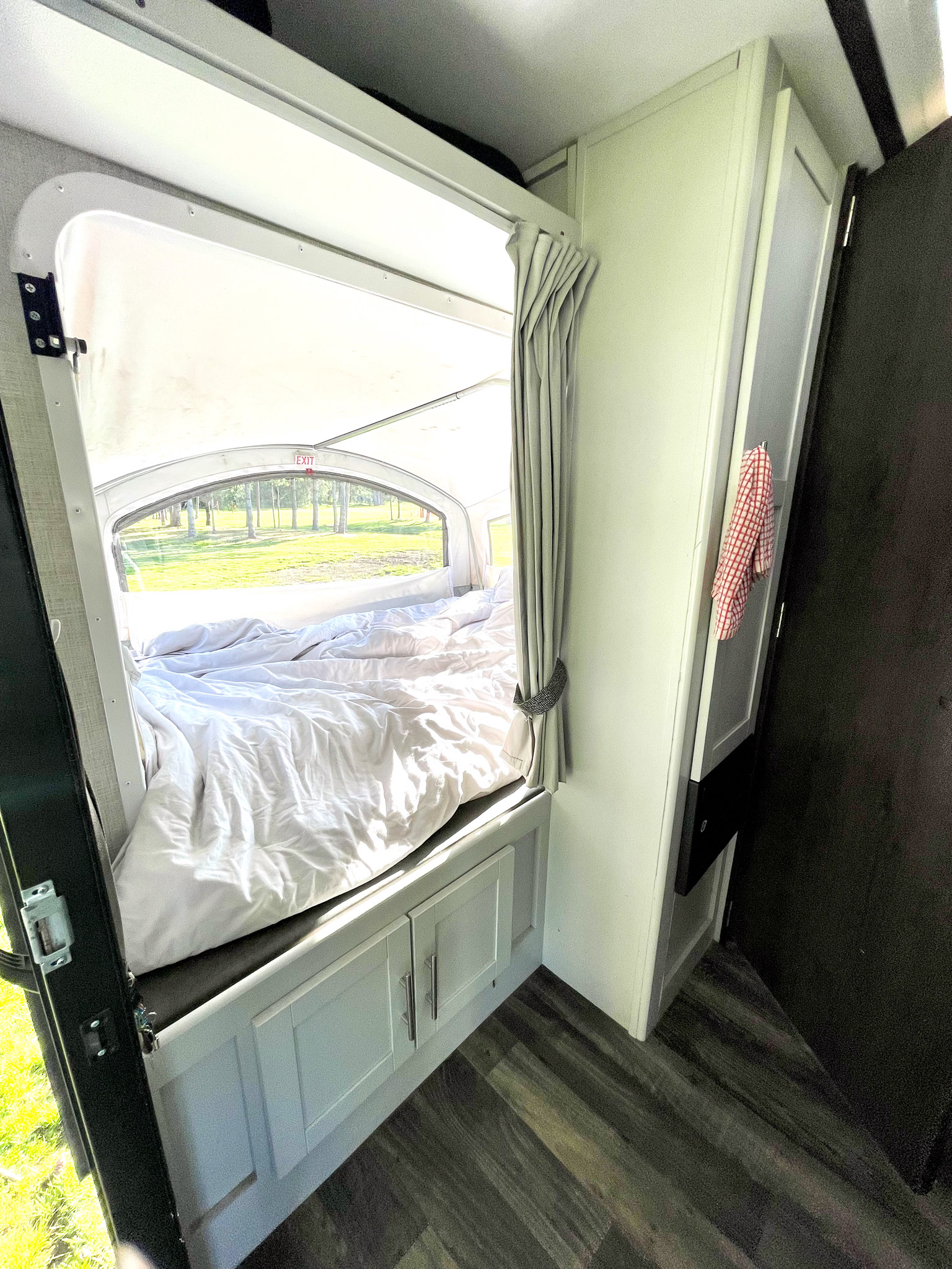 This RV rental shows a cozy bedroom with a large window offering a scenic view of trees and grass. Features a bed with white bedding and storage cabinets.. Keystone RV Bullet Crossfire 2019