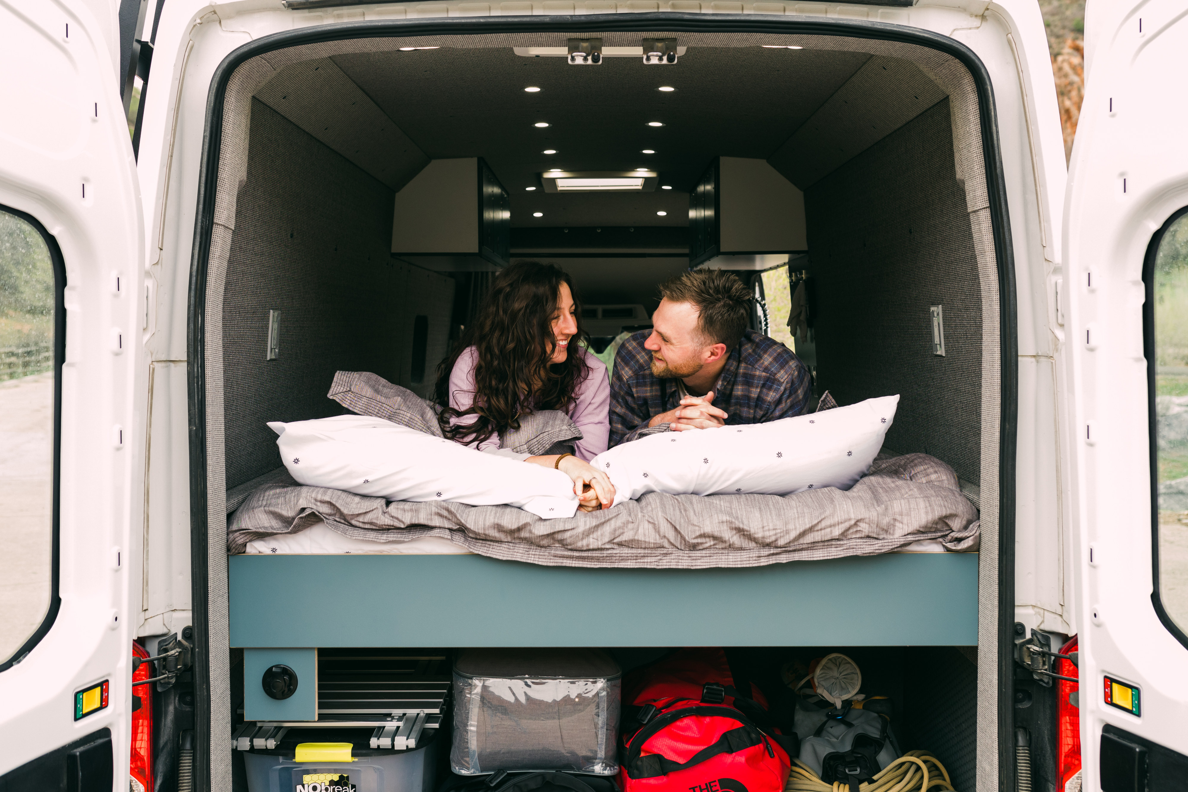 Cozy RV rental van interior with a smiling couple on the bed, enjoying their van life adventure.. Ford Transit 250 RWD 2018