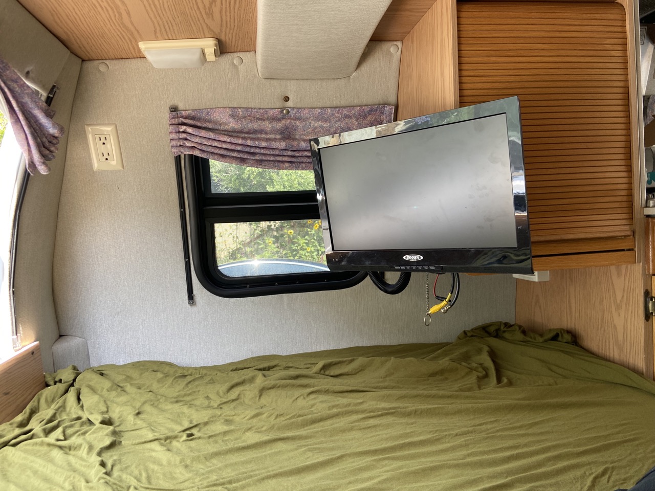 Cozy RV rental interior features a green bed, mounted TV, and window. Ideal compact living space.. Roadtrek 190 Versatile 2003
