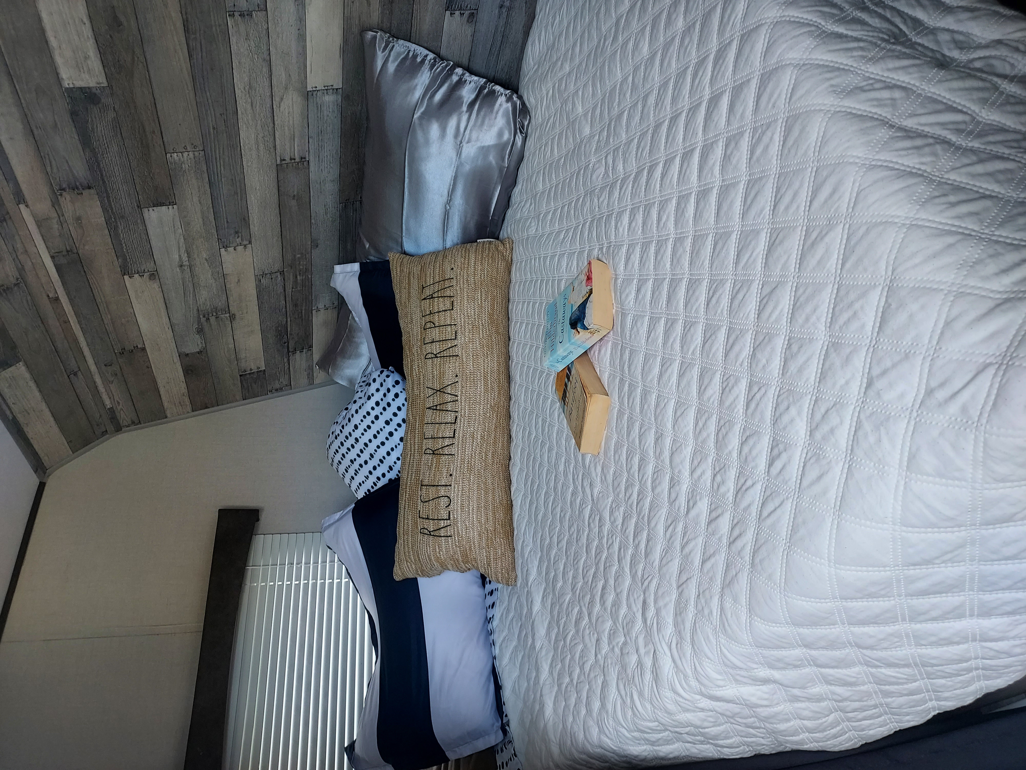 Cozy RV rental bedroom featuring a quilted bed, themed pillows, books, and rustic wood-paneled walls.. Crossroads RV Zinger Lite 2022