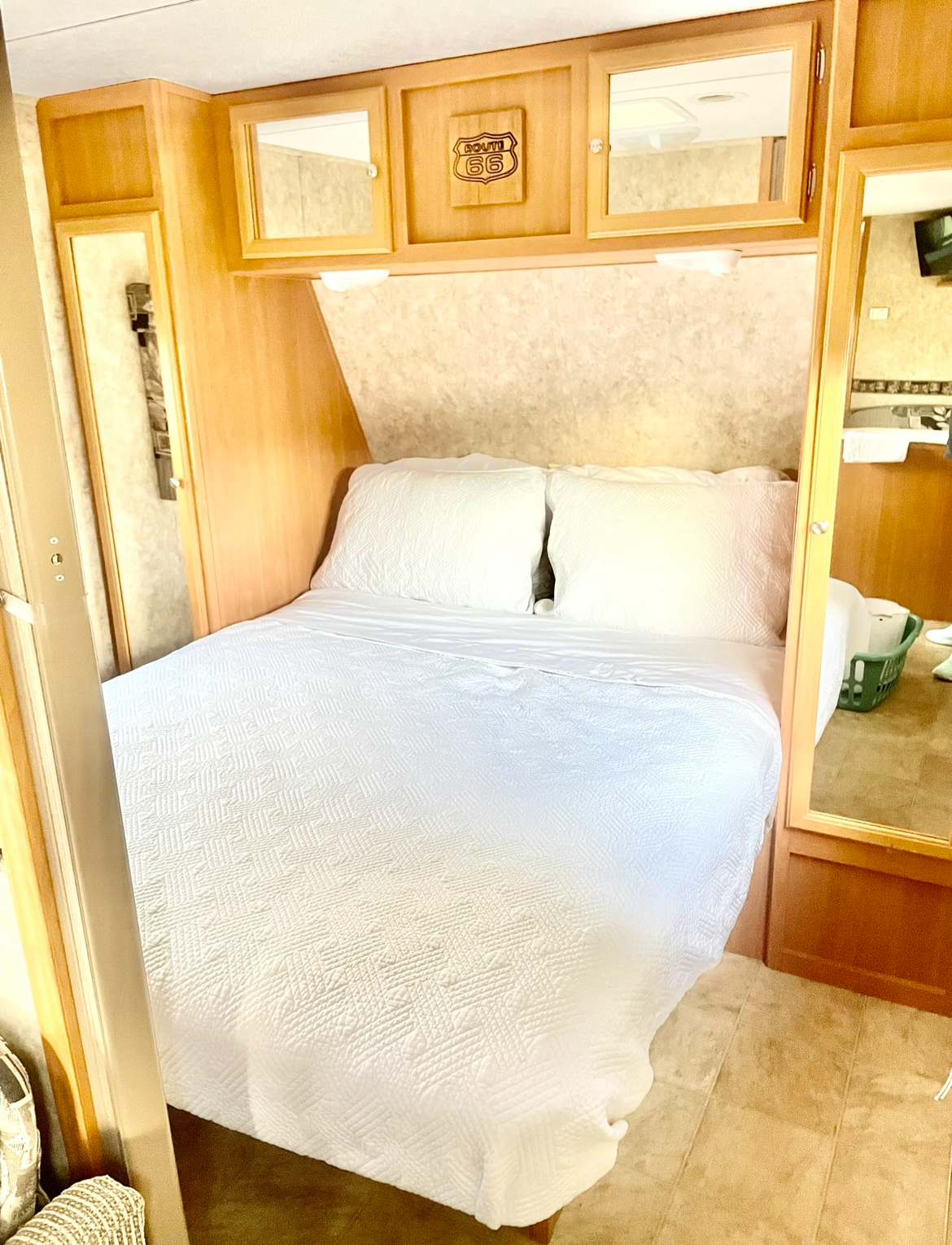 Enjoy a comfortable RV rental bedroom featuring a clean white bed, wood cabinets, and Route 66 decor.. RTFLY CCH 2007