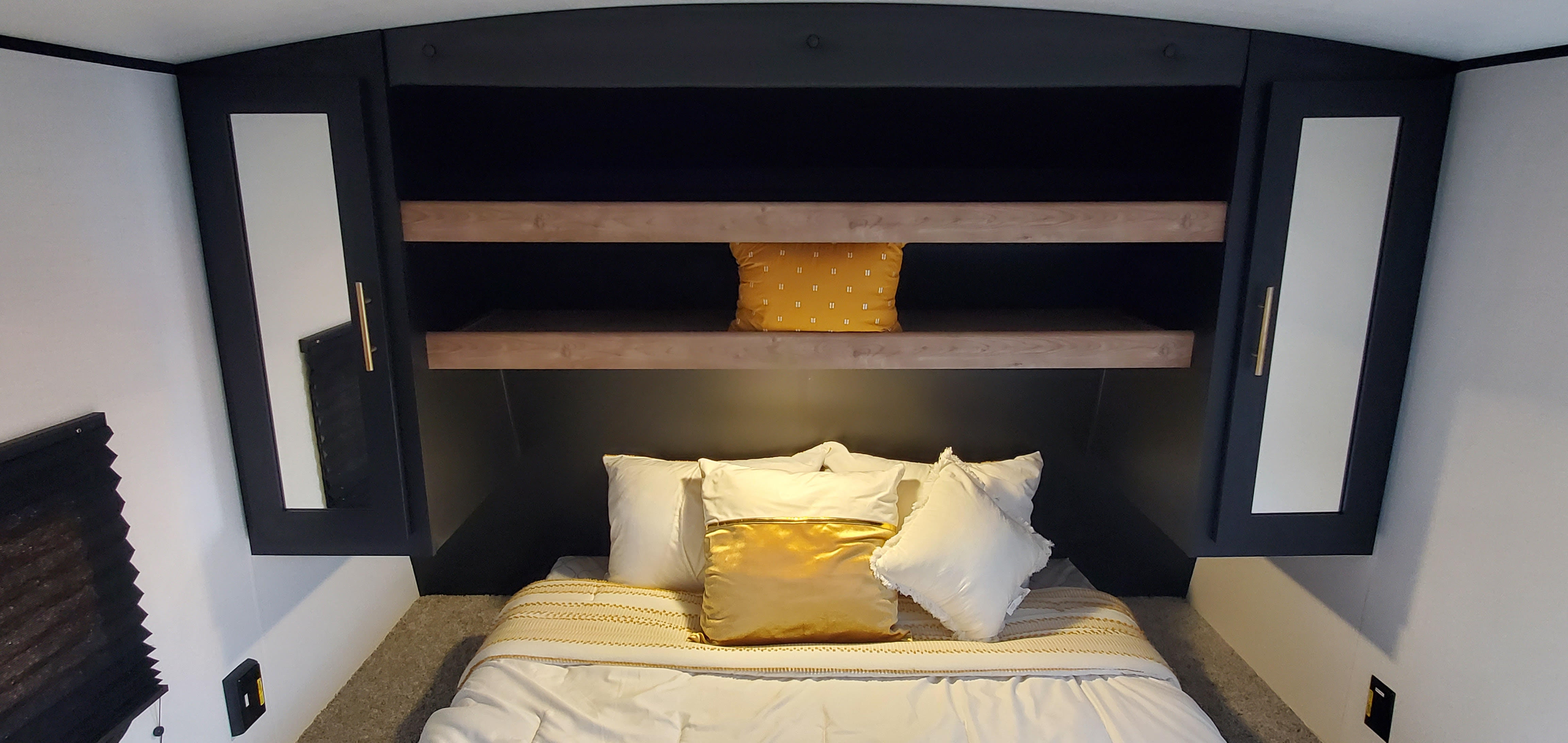 Compact RV rental bedroom featuring overhead storage, built-in wooden shelves, and cozy white/gold bedding.. Keystone RV Springdale 2022