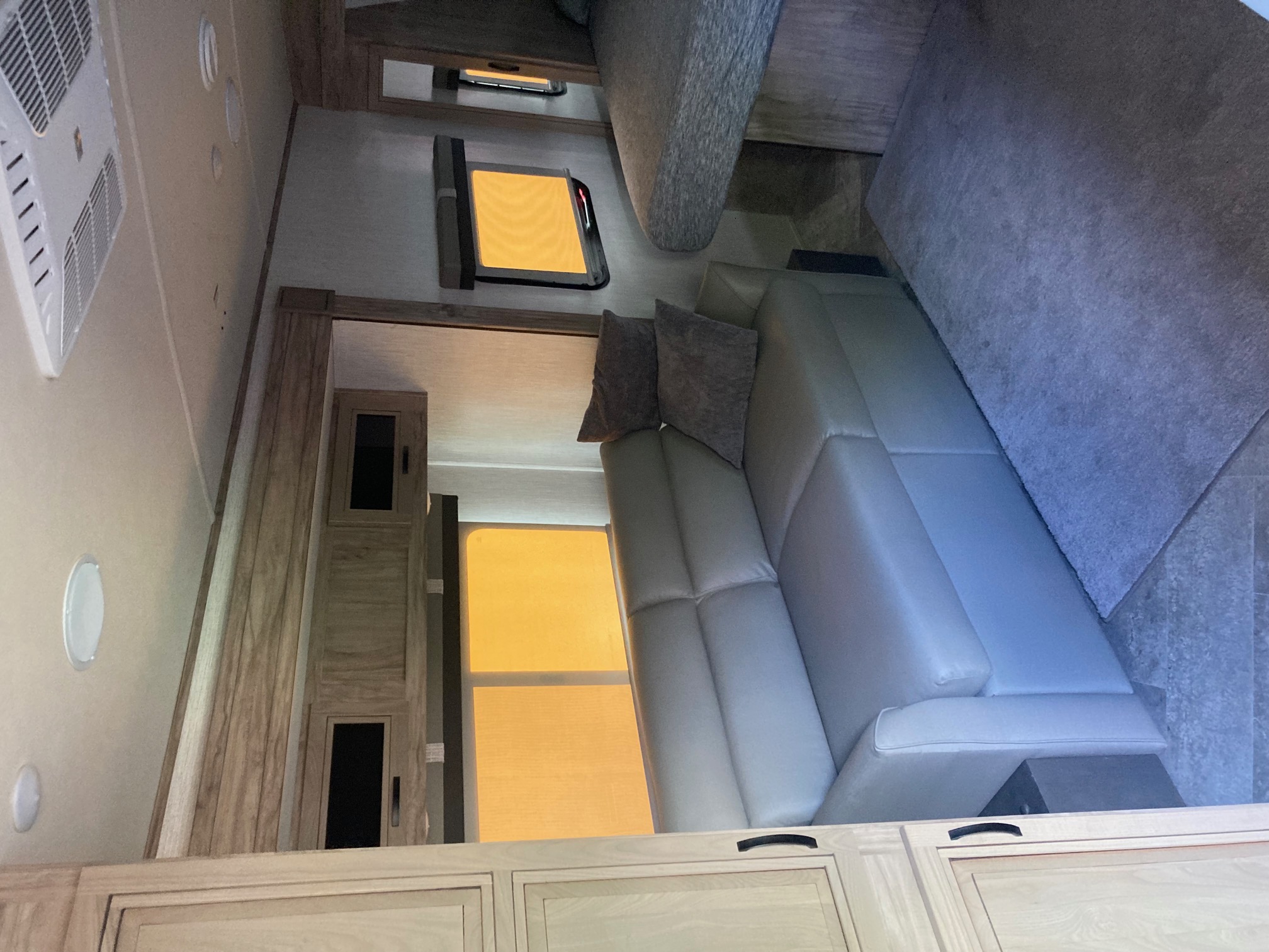 Spacious RV rental interior featuring a light-colored couch, bed, and wooden cabinetry, creating a comfortable living area.. Forest River Palomino Solaire 2021