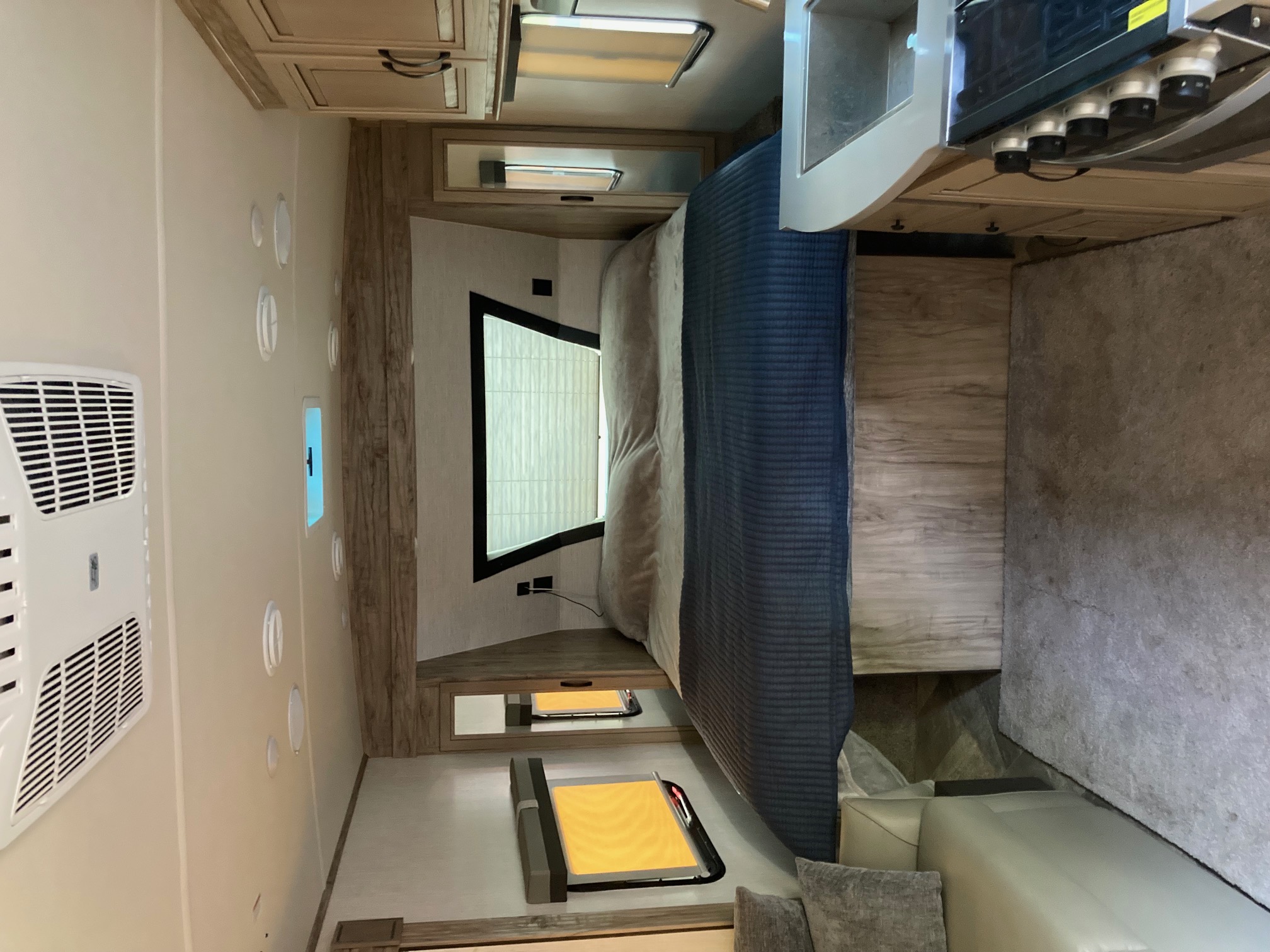 Explore this modern **rv rental** bedroom with a comfy bed, overhead storage, AC, and bright window, extending to a cozy living area.. Forest River Palomino Solaire 2021