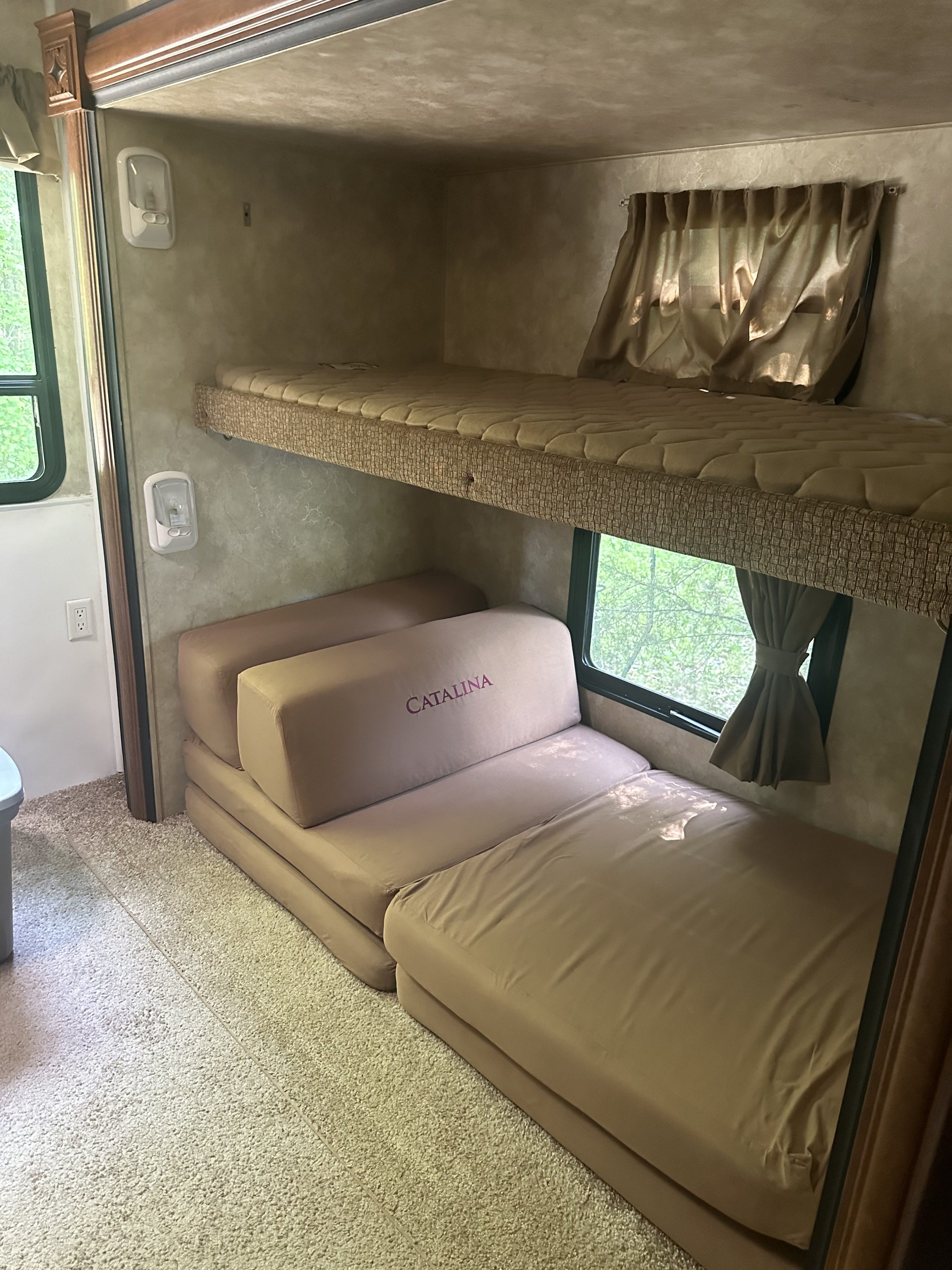 RV rental interior featuring bunk beds and a foldable sofa bed next to a window with nature views, on a carpeted floor.. Coachmen Catalina 2013
