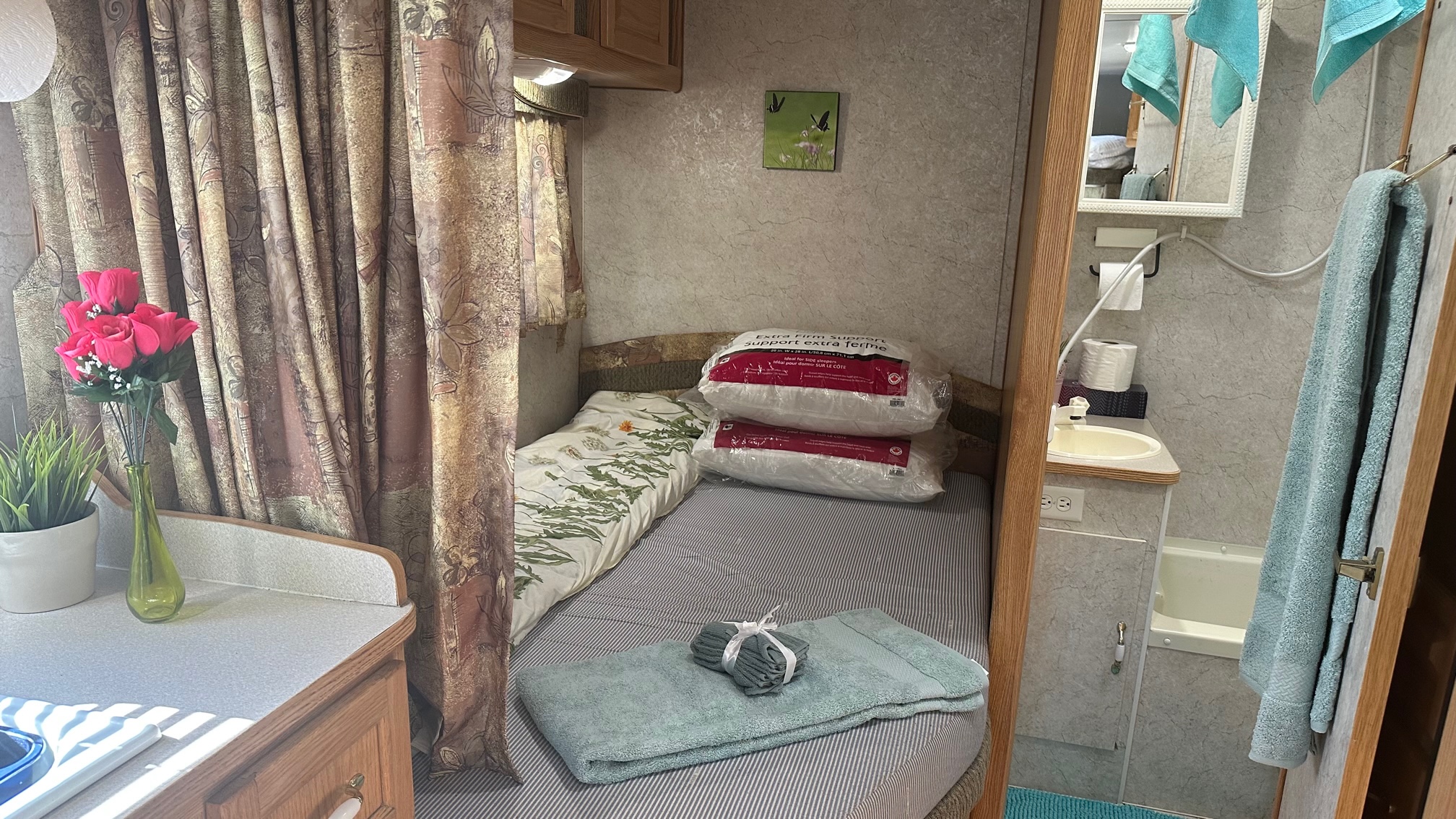 A cozy RV rental interior showcasing a compact bedroom with a bed, pillows, and a small bathroom with sink and tub.. Adventurer Adventurer Motorhome 2005