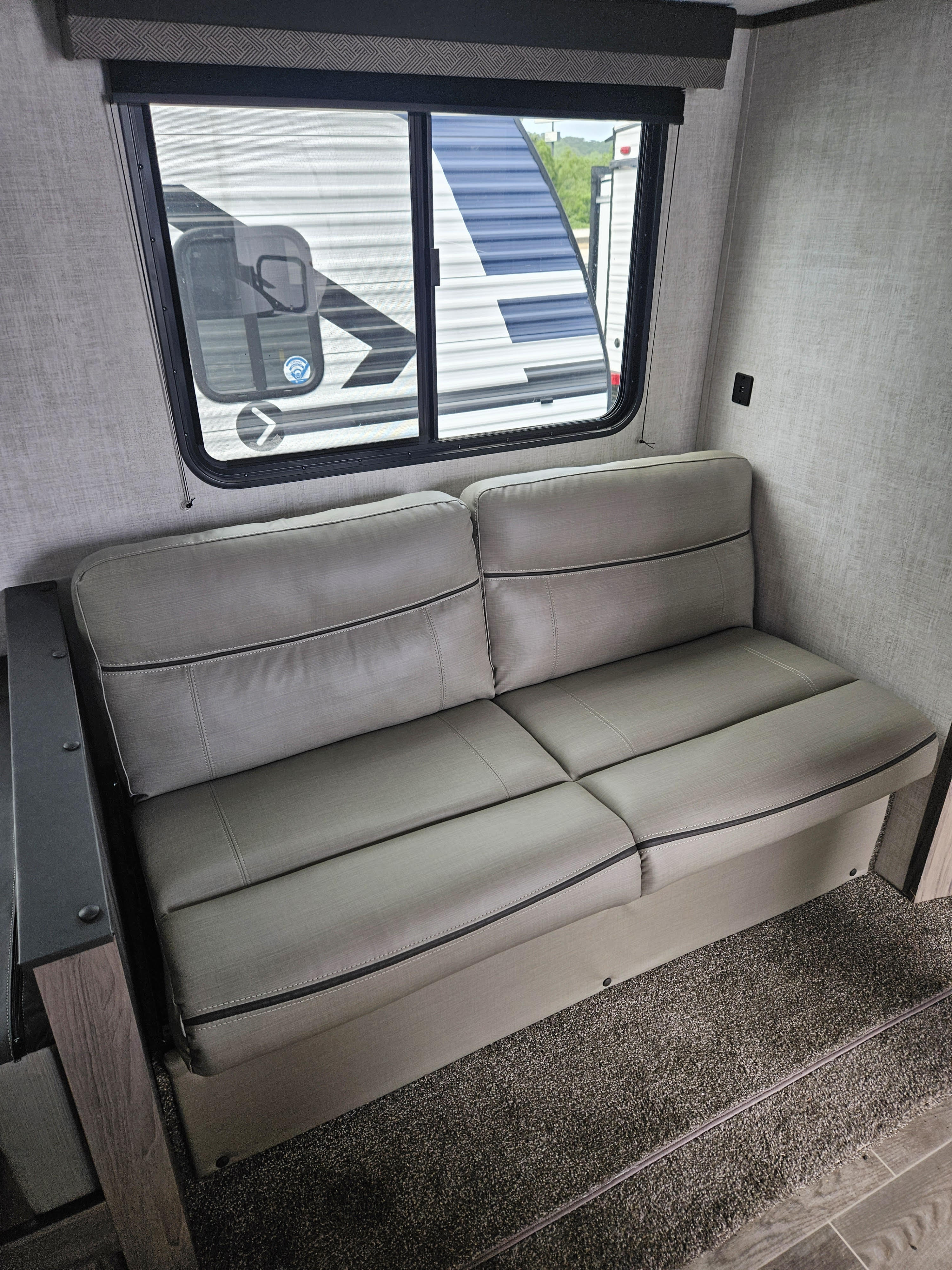 RV rental's cozy interior: modern grey sofa with contrast stitching by a bright window, showcasing a clean, comfortable space.. Gulf Stream Ameri-Lite 2022