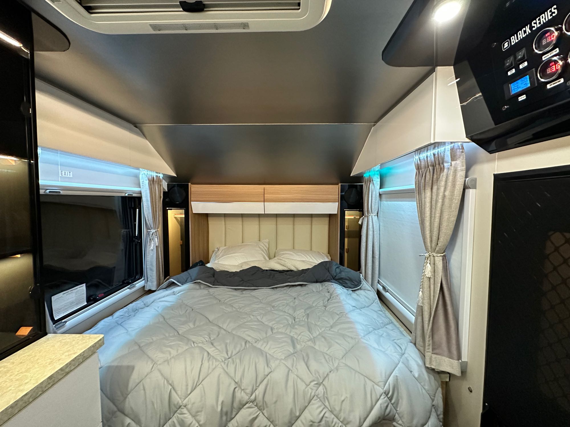 Spacious RV rental bedroom showcasing a comfortable bed, overhead cabinets, and a modern control panel.. Black Series Black Series Trailer 2022