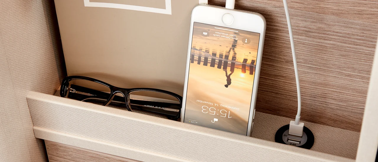 An RV rental's clever storage: eyeglasses, charging iPhone, and a built-in USB port for travel convenience.. Bürstner campeo 540 2023