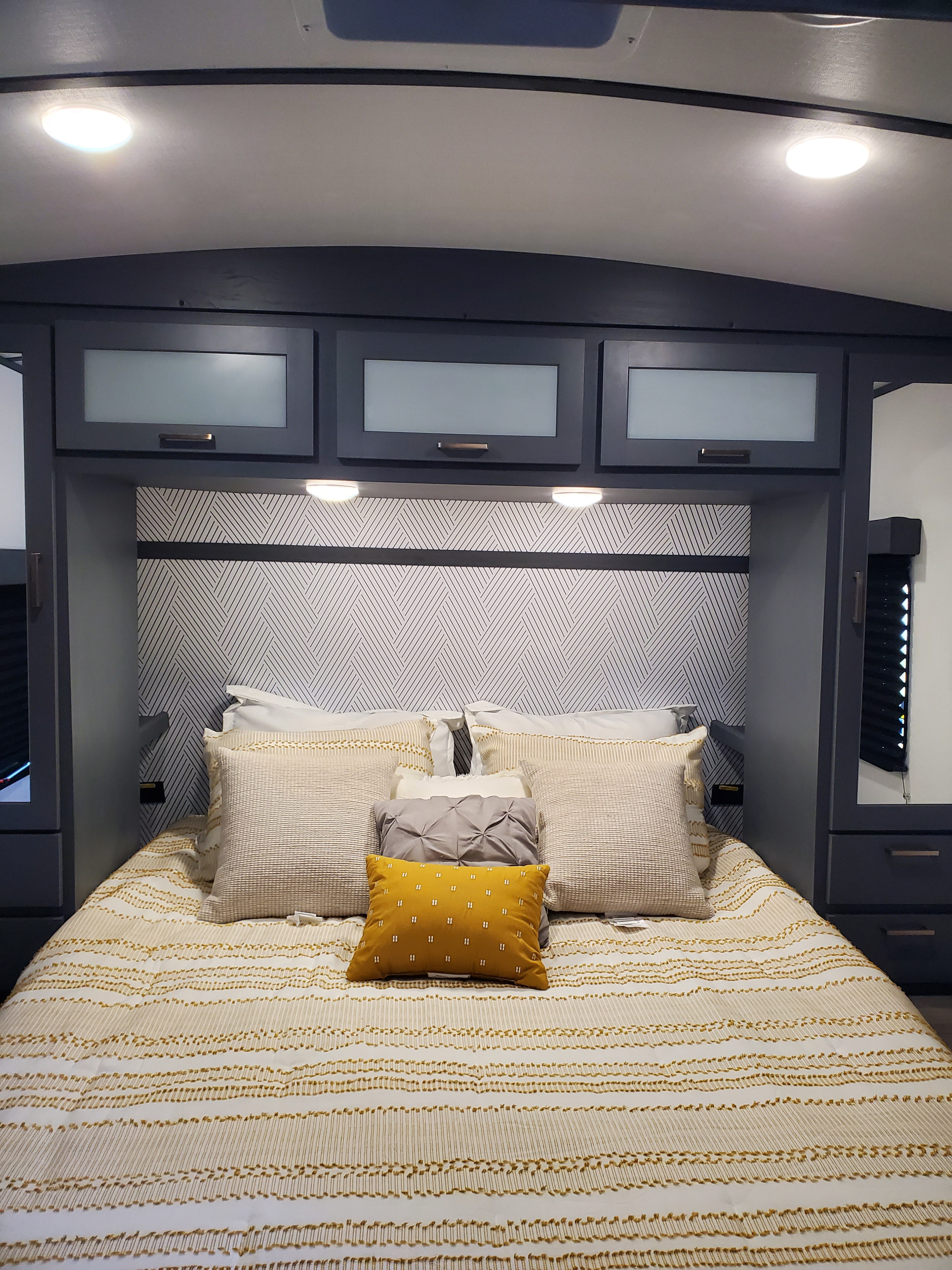 Cozy RV rental bedroom featuring a patterned headboard, ample storage, and stylish bedding in cream, yellow, and grey tones.. Keystone RV Bullet Ultra Lite 2023