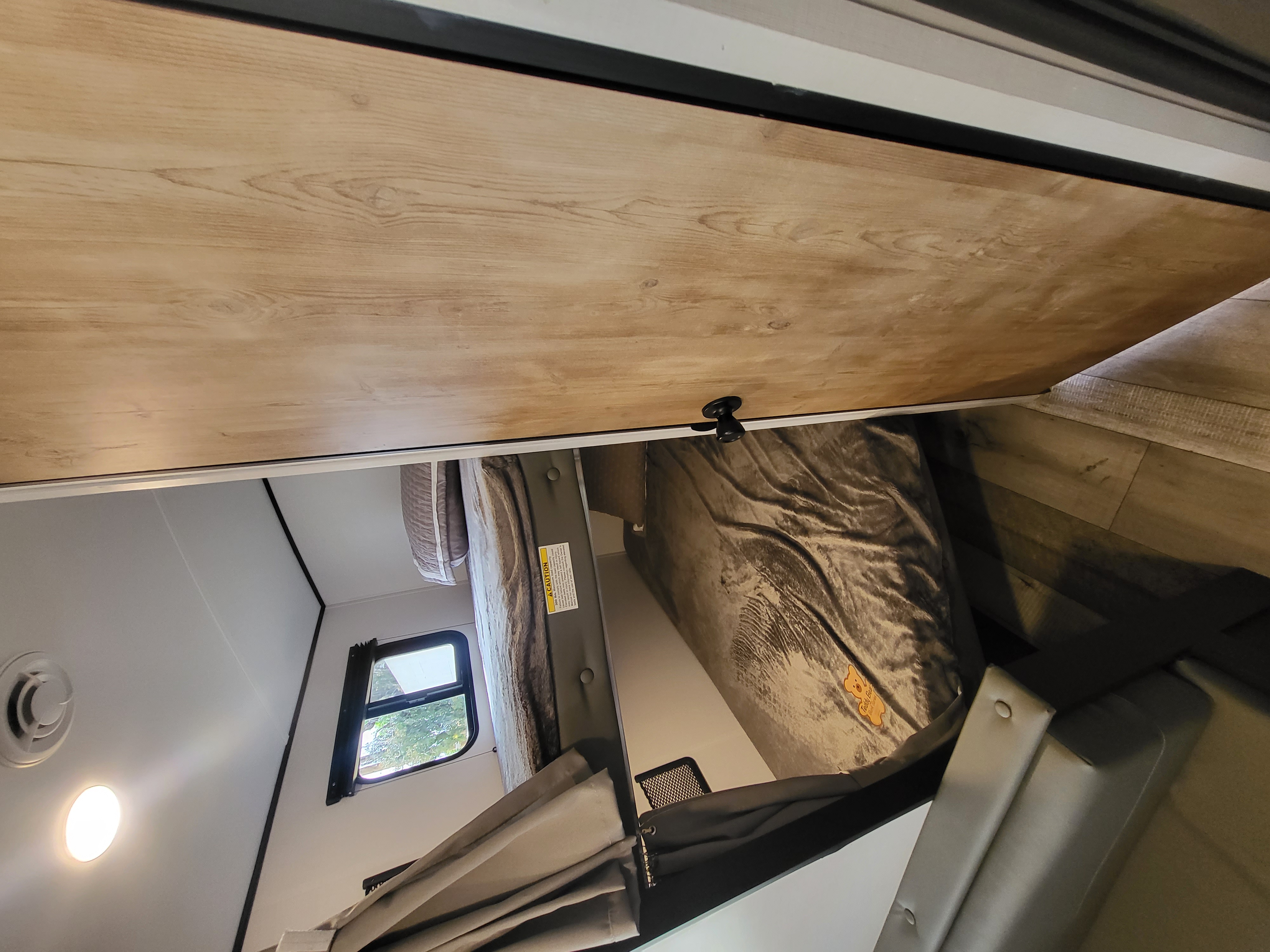 View inside an RV rental bunk area, showing the wooden underside of an upper bunk, a cozy lower bed, window, and light.. Keystone RV Springdale 2022