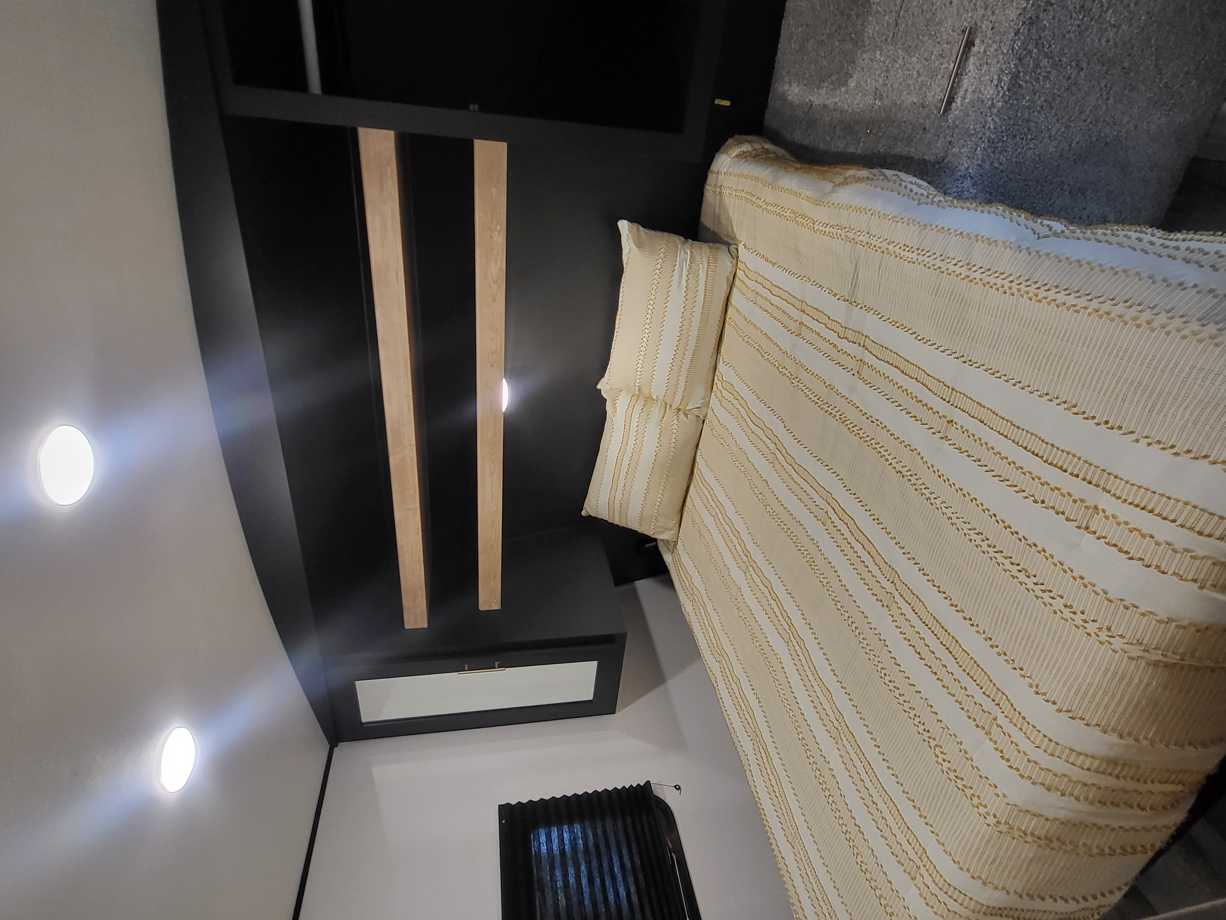 Modern RV rental bedroom with cream bedding, sleek black headboard, and wood accents.. Keystone RV Springdale 2022