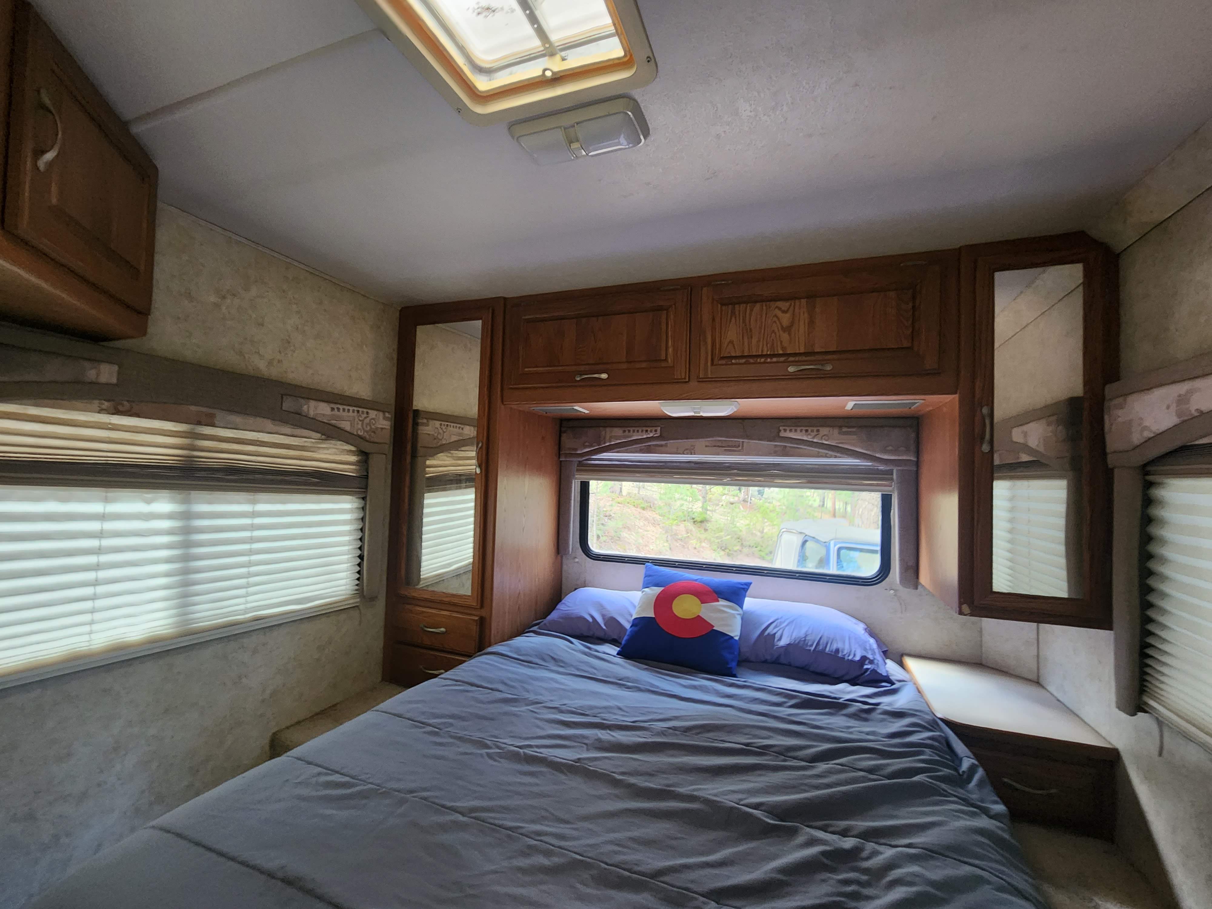 Cozy RV rental bedroom: a comfortable bed with a Colorado pillow, wooden cabinets, windows, and a ceiling skylight.. Four Winds Chateau 2004