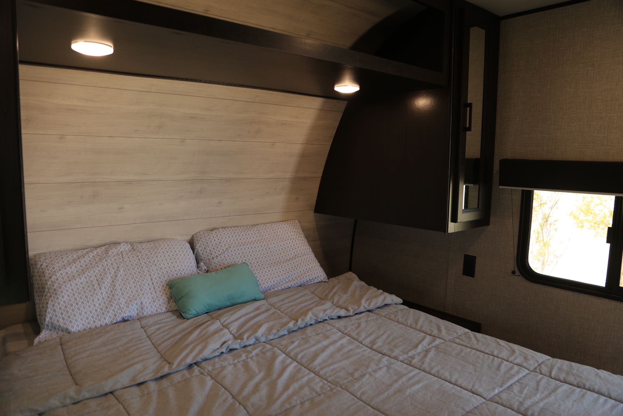 Modern RV rental bedroom with comfy bed, wood headboard, and overhead lights for a cozy stay.. Jayco Jay Flight 2023