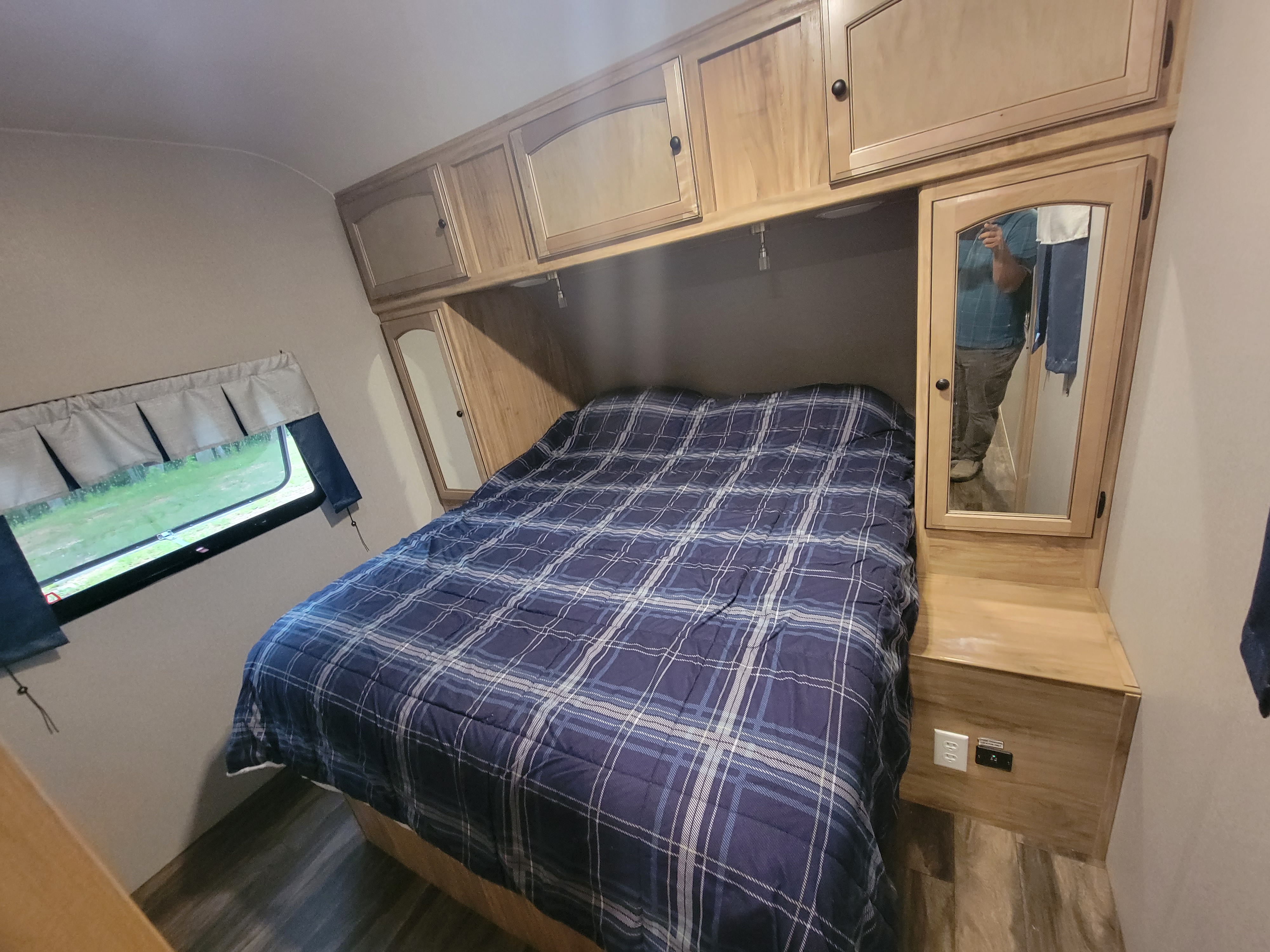 Interior of an RV rental bedroom, featuring a blue plaid bed, wooden cabinets, and a mirrored closet.. Coachmen Freedom Express 323bhds 2019