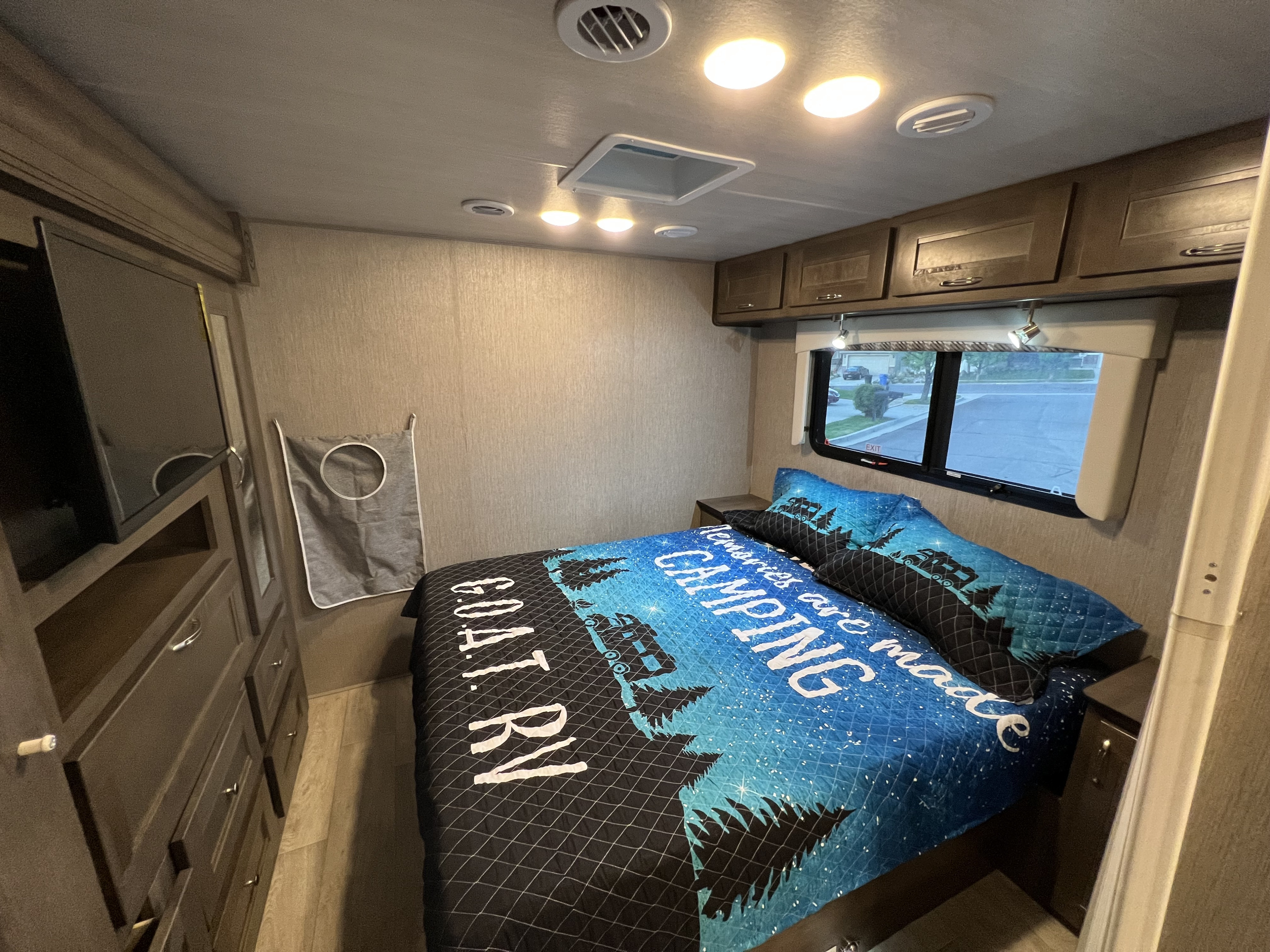 Cozy RV rental bedroom with a camping-themed bed, TV, and storage. Bright interior with window view, ready for adventures.. Nexus RV Triumph 2022