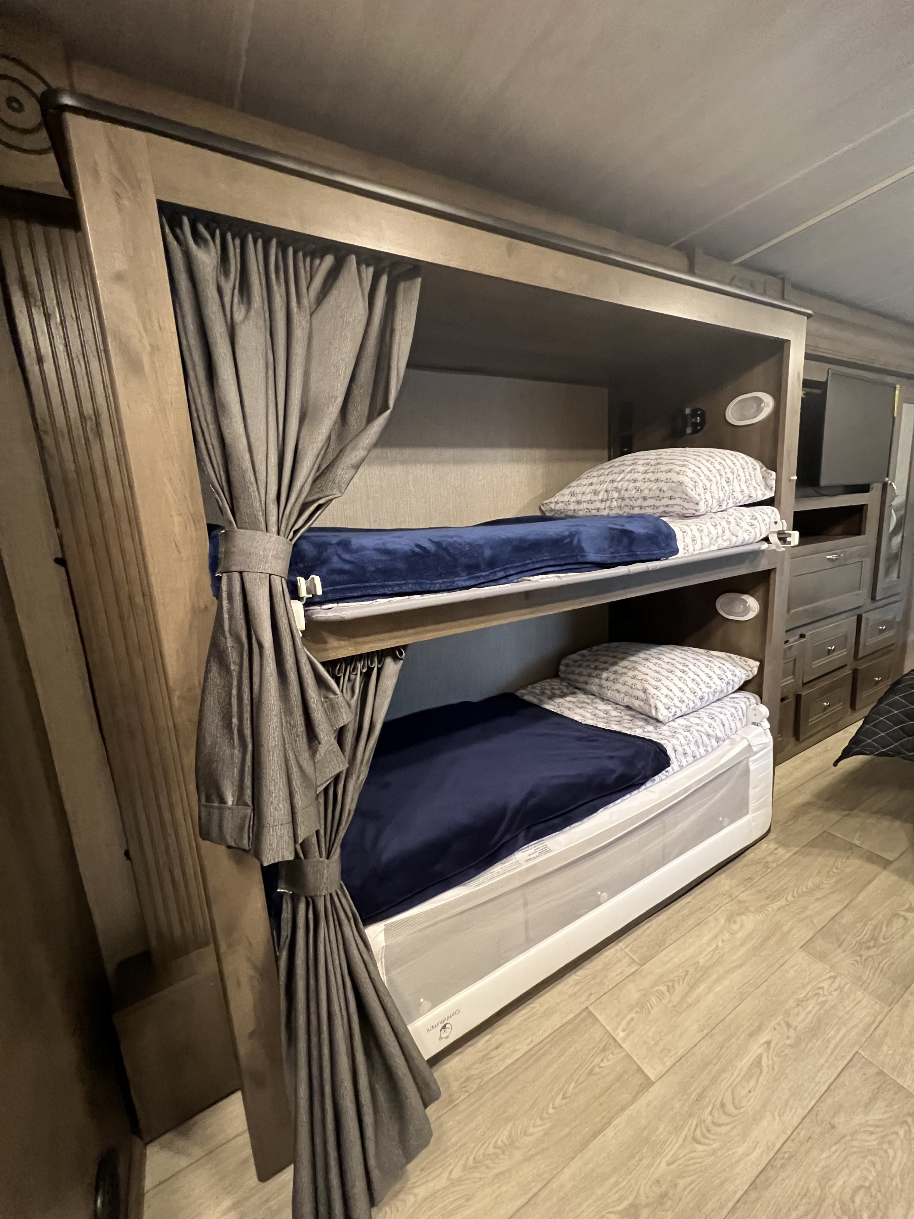 Stacked bunk beds in RV rental, featuring privacy curtains, blue blankets, and reading lights.. Nexus RV Triumph 2022
