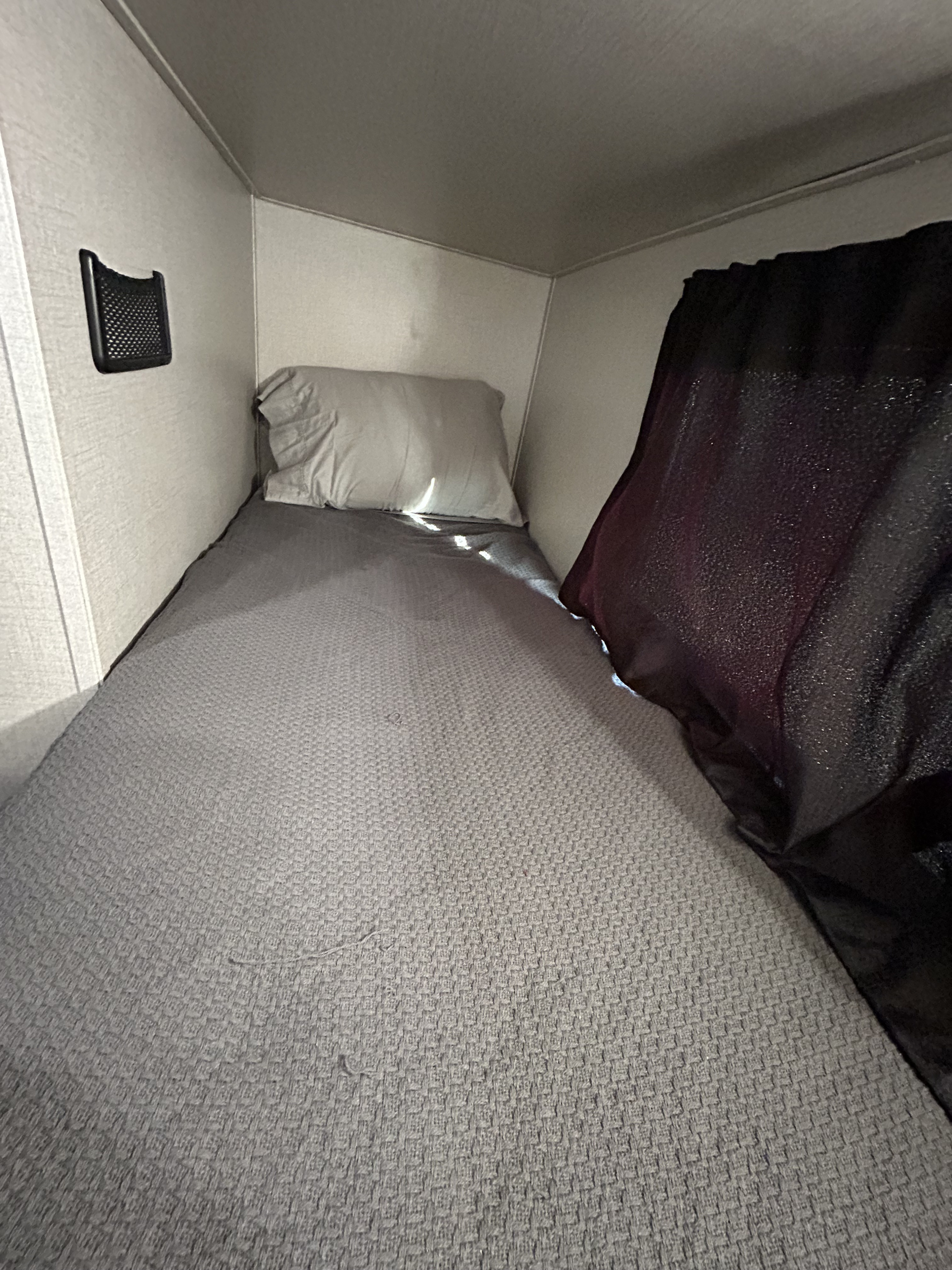 Compact sleeping area in an RV rental: a grey bed with pillow, wall-mounted mesh storage, and dark curtain.. Olympia Sport 2022
