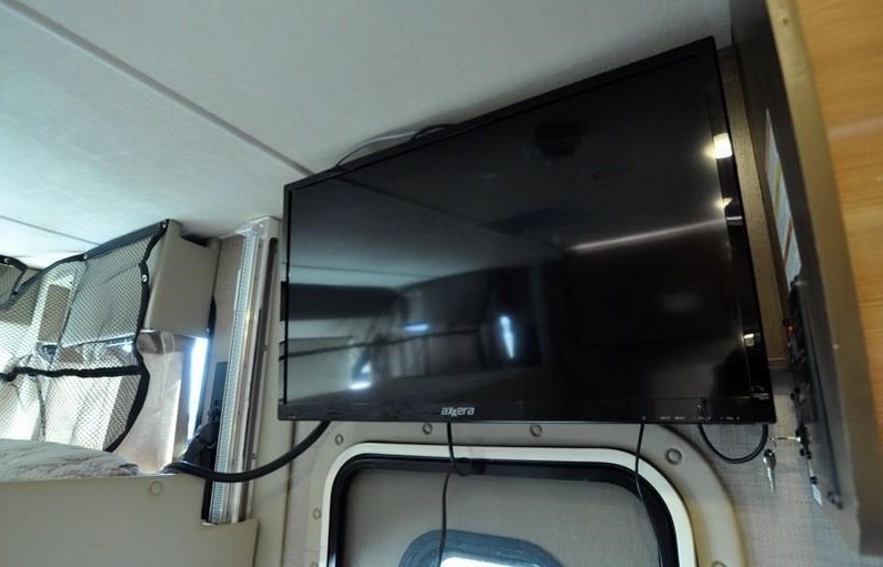 RV rental interior featuring a flat-screen TV mounted above a distinctive round window, offering entertainment and comfort on trips.. Thor Axis 2018