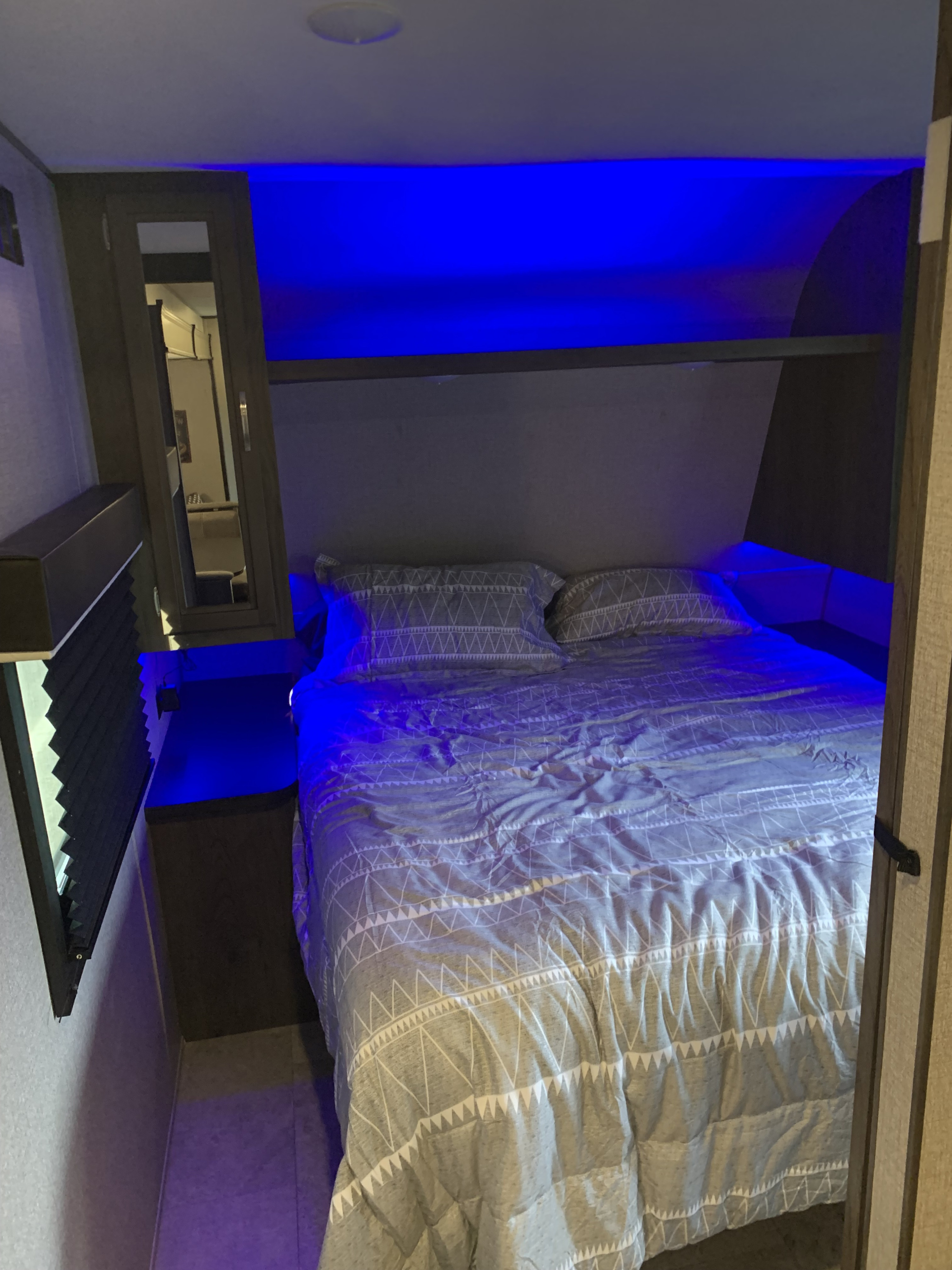 RV rental interior: cozy bedroom featuring blue accent lights, patterned bedding, and a side window.. Jayco Jay Flight SLX Rocky Mountain Edition 2020