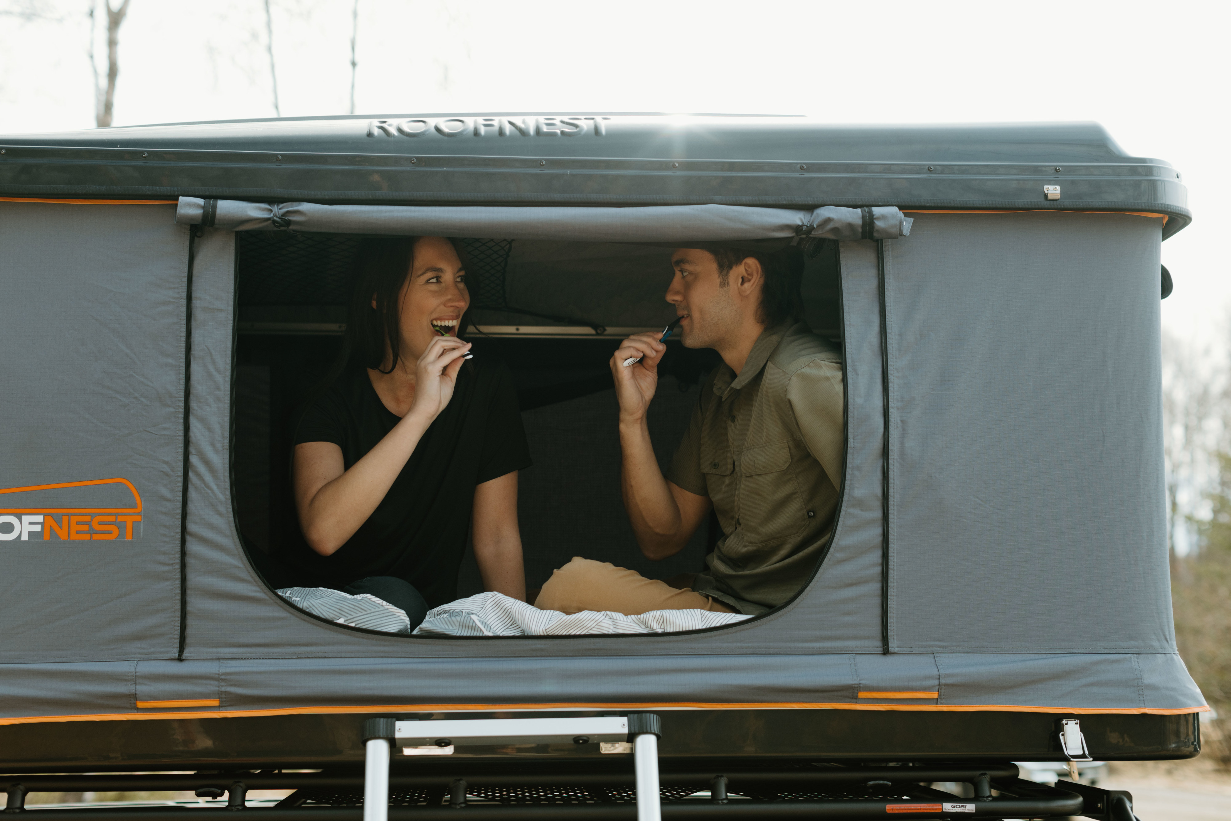 Couple brushing teeth inside a Roofnest rooftop tent. A comfortable camping option for your rv rental.. Jeep Wrangler 2023