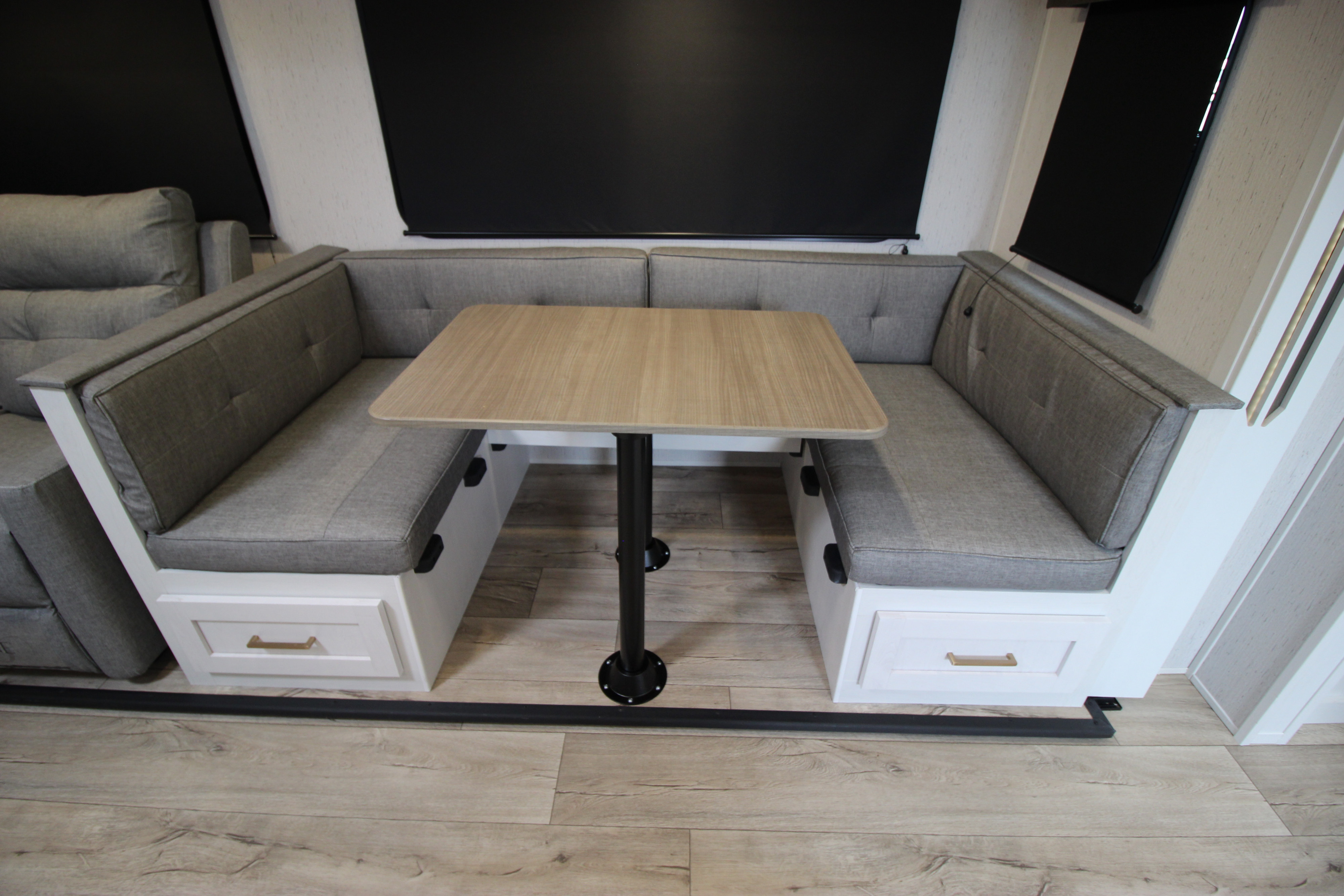 This RV rental interior showcases a comfortable U-shaped dinette with gray cushions, a light wood table, and built-in storage.. Dutchmen Astoria 2023