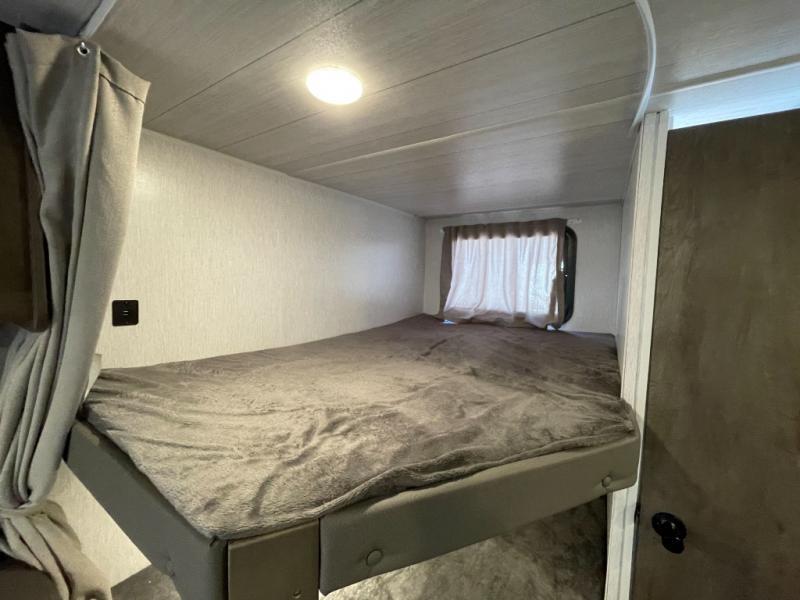 RV rental bunk bed setup with soft grey bedding, a side curtain, and a window, offering a cozy sleeping space.. Forest River Salem Cruise Lite 2022