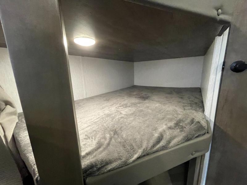 Cozy bunk bed in RV rental, with soft gray blanket & ceiling light. A comfortable sleeping spot for your trip.. Forest River Salem Cruise Lite 2022