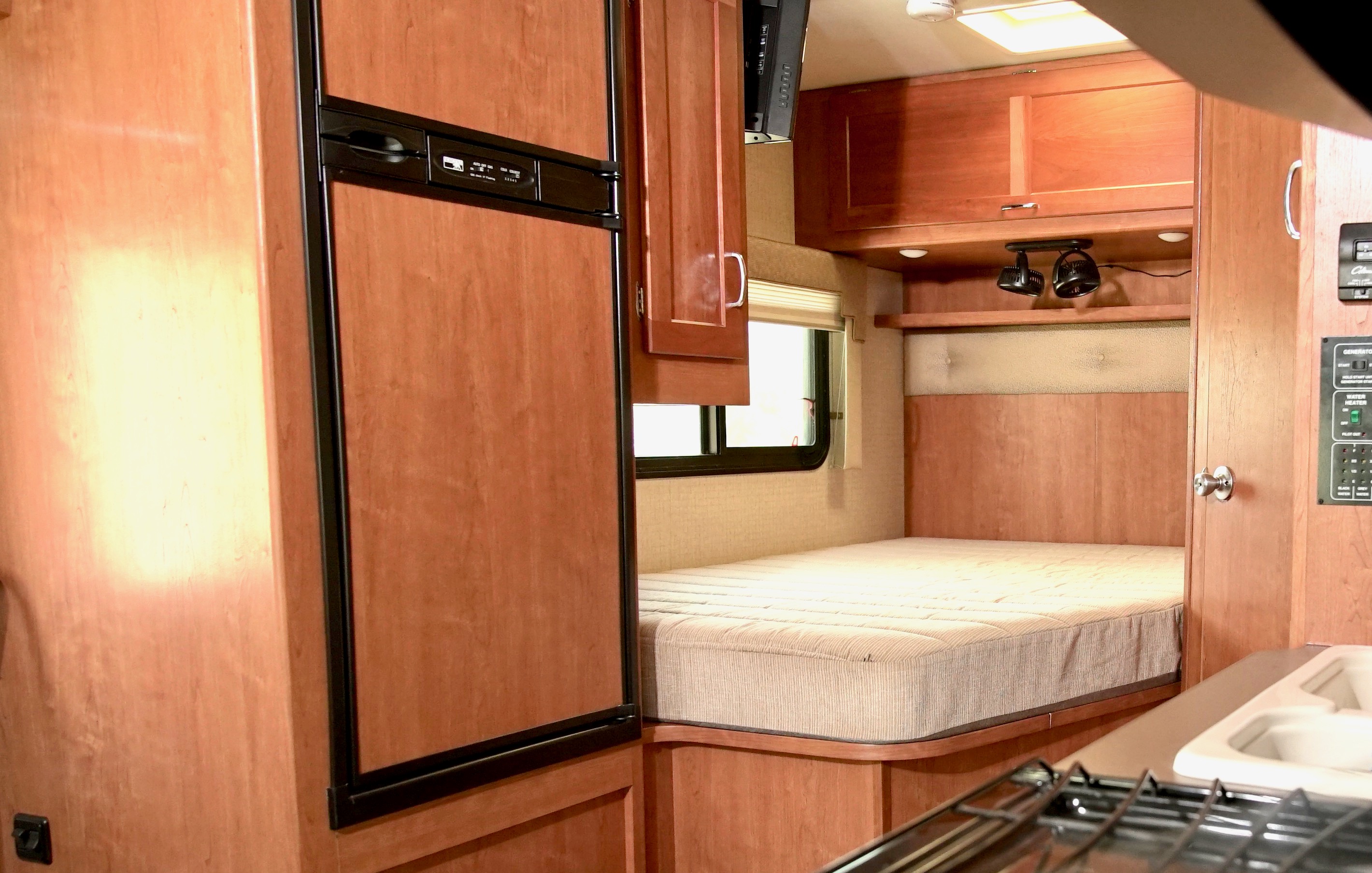 Cozy RV rental interior: bedroom area with bed, window, storage, fridge, and partial kitchen view.. Winnebago Minnie Winnie 2017