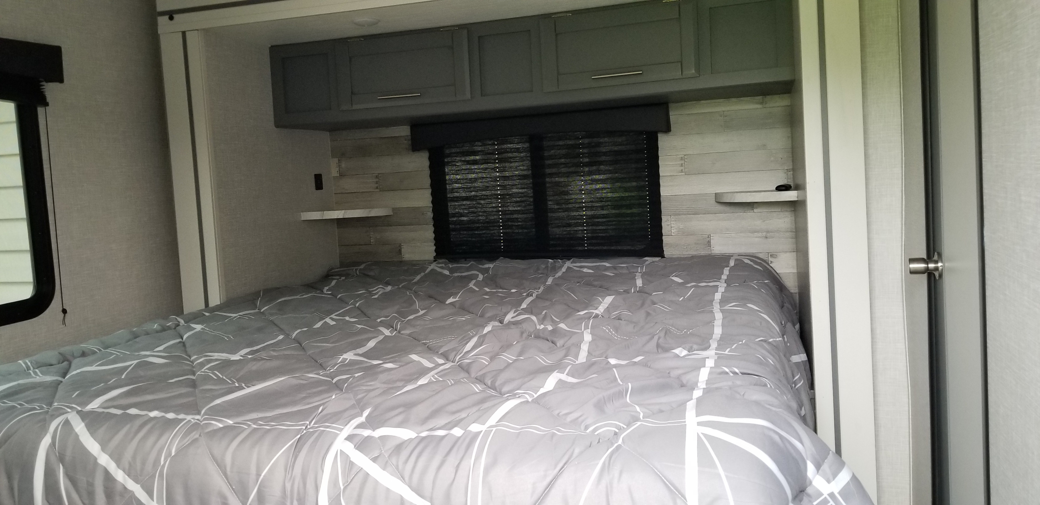 Inviting rv rental bedroom showing a comfortable bed with gray comforter, sleek overhead cabinets, and a rustic shiplap accent wall.. Crossroads RV Volante 2022