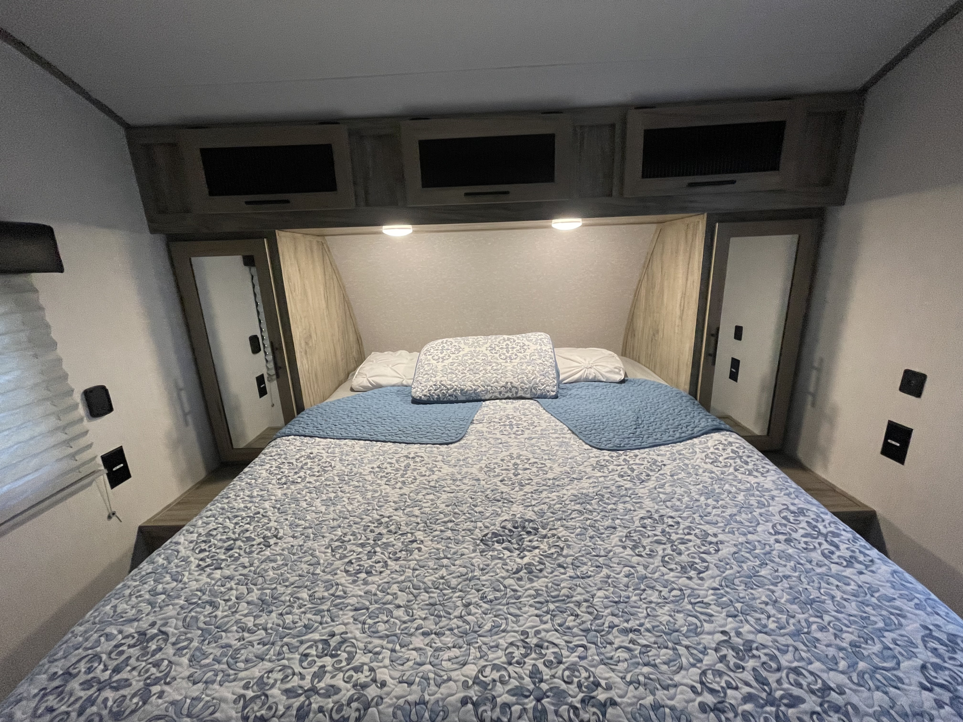 Cozy RV rental bedroom featuring a queen bed with blue patterned bedding, overhead storage, and bedside outlets.. Forest River Cherokee 2022
