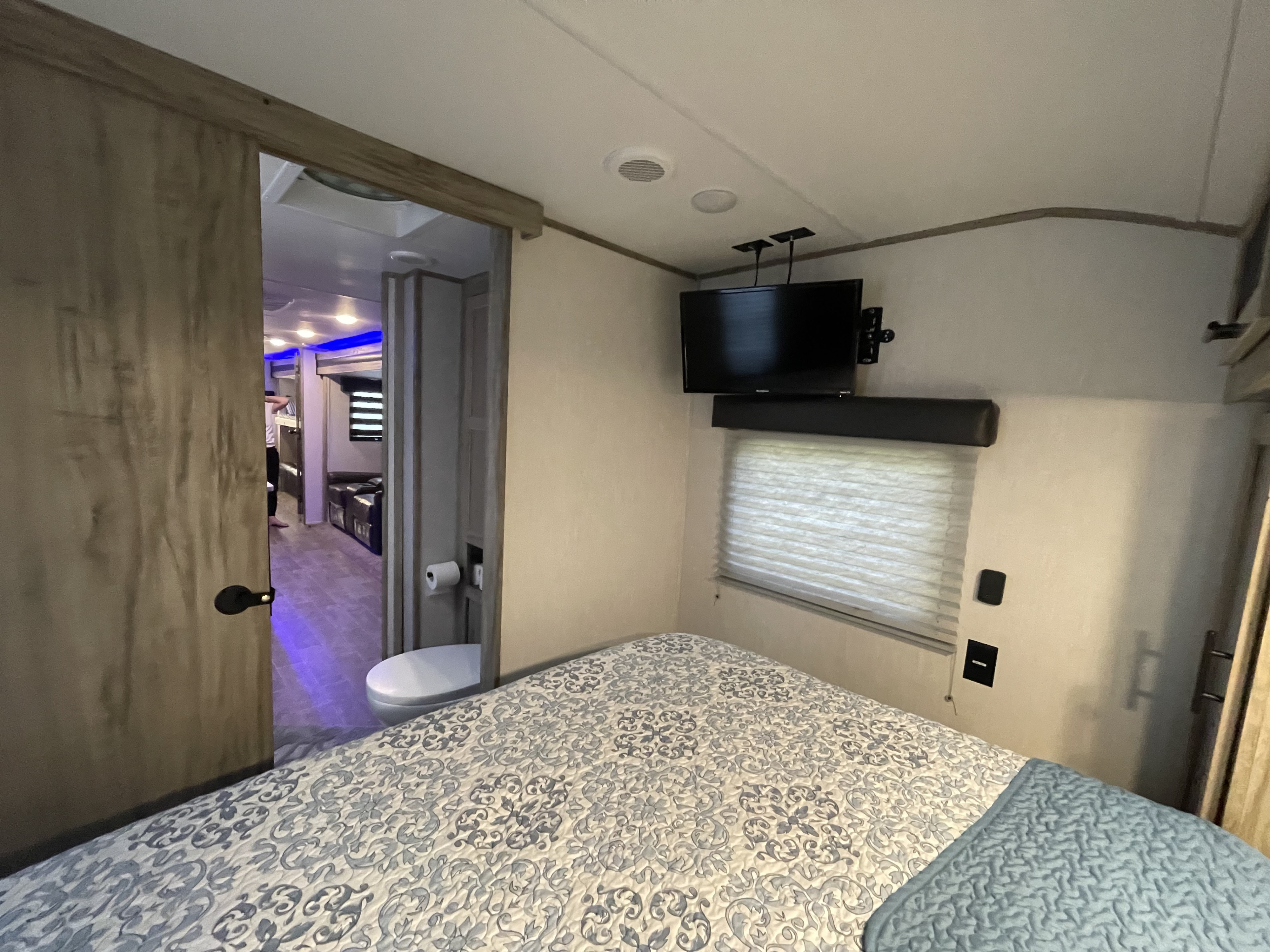 RV rental showcasing a well-appointed bedroom with TV and window, leading to a compact bathroom and illuminated living space.. Forest River Cherokee 2022