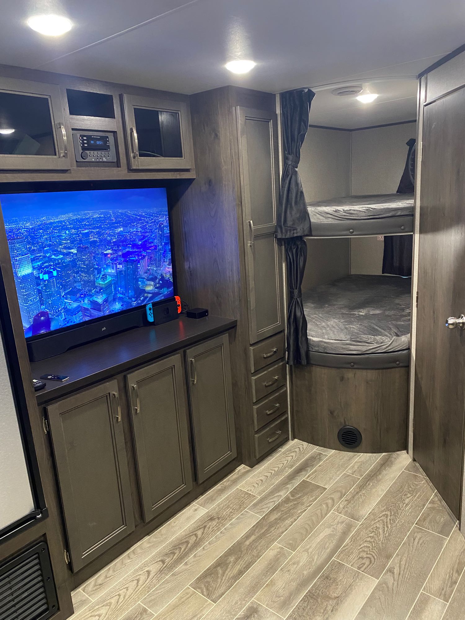 This RV rental's interior boasts a large TV with gaming setup, entertainment center, and comfortable bunk beds with privacy curtains.. Jayco Jay Flight 2021