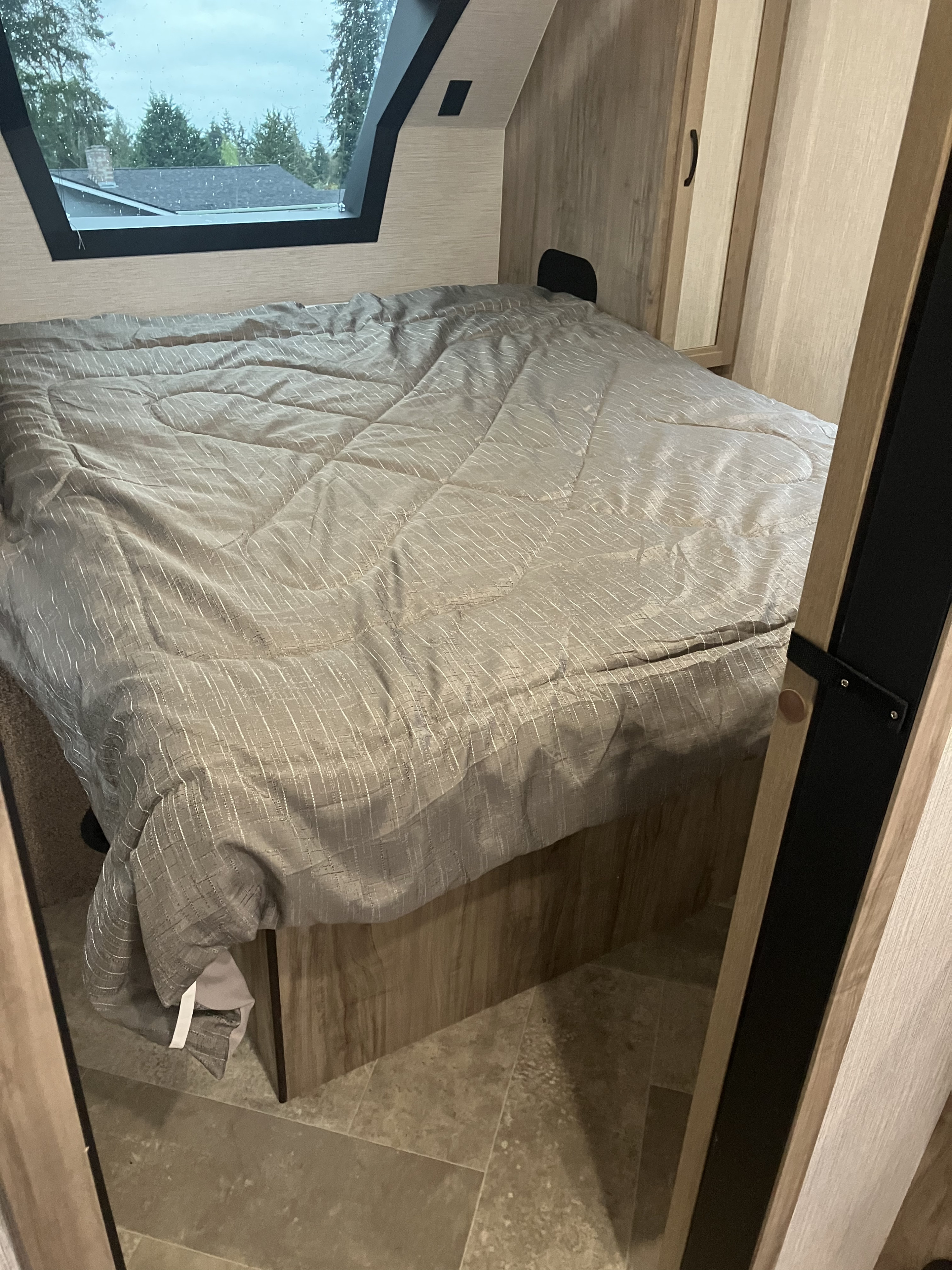 Inside an RV rental, a bedroom features a grey comforter on a bed, wooden walls, and a large window view.. Forest River Palomino Solaire 2022
