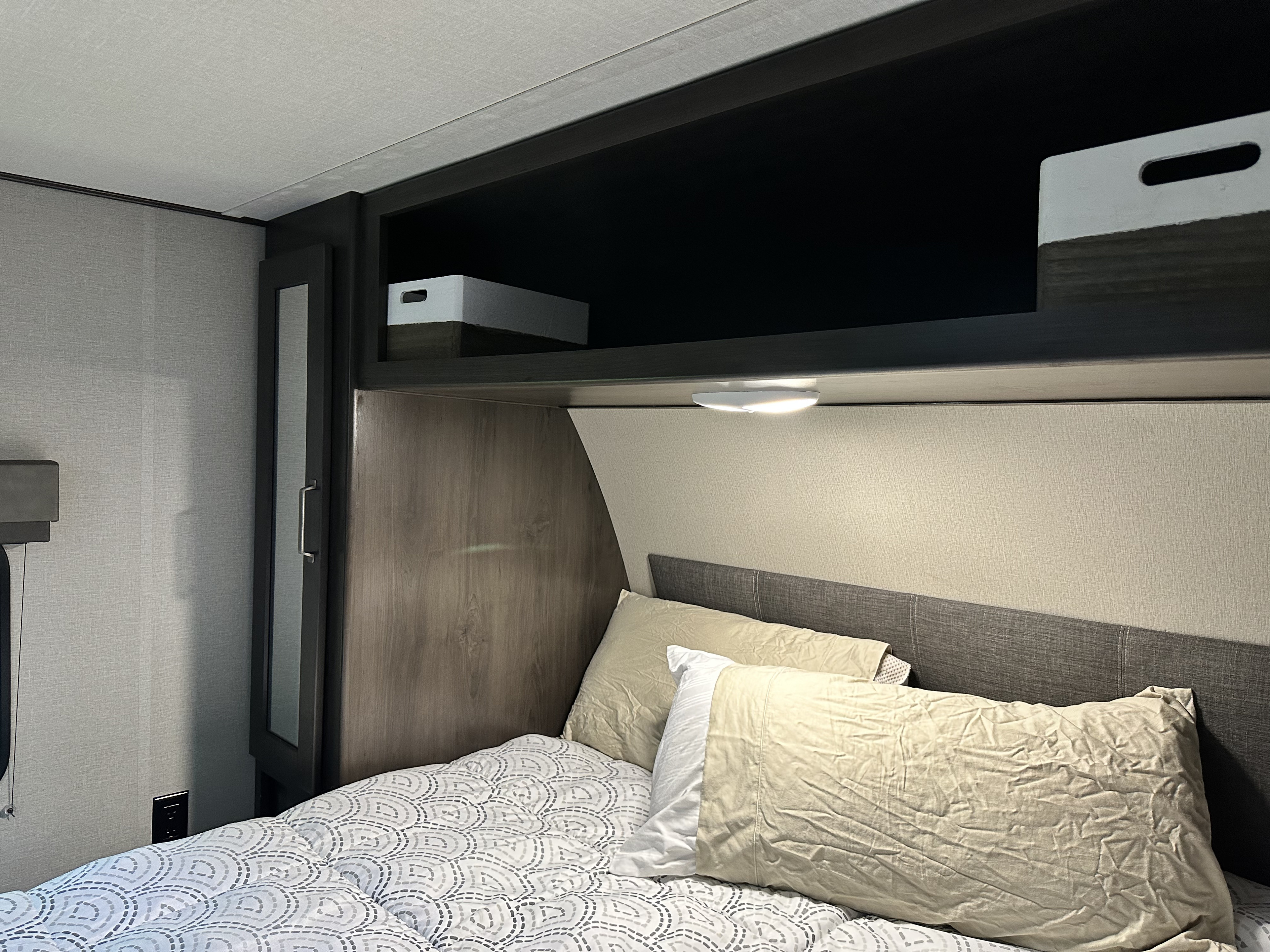 Well-appointed RV rental bedroom with a comfortable bed, patterned comforter, overhead storage, and reading light.. Grand Design Transcend Xplor 2022