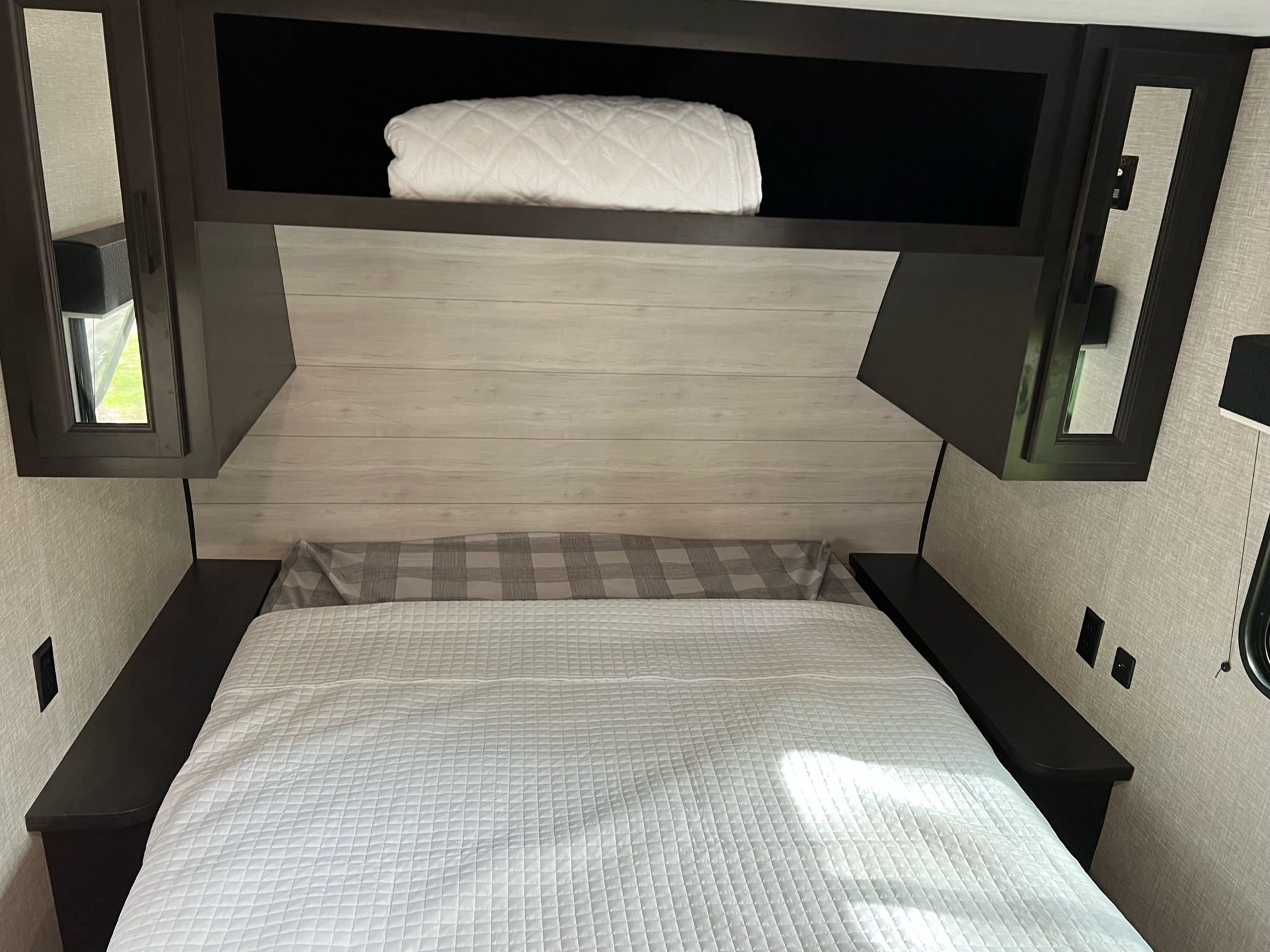 RV rental bedroom view: a neatly made bed with white bedding, overhead storage with a blanket, and convenient side shelves.. Jayco Jay Flight SLX 2022