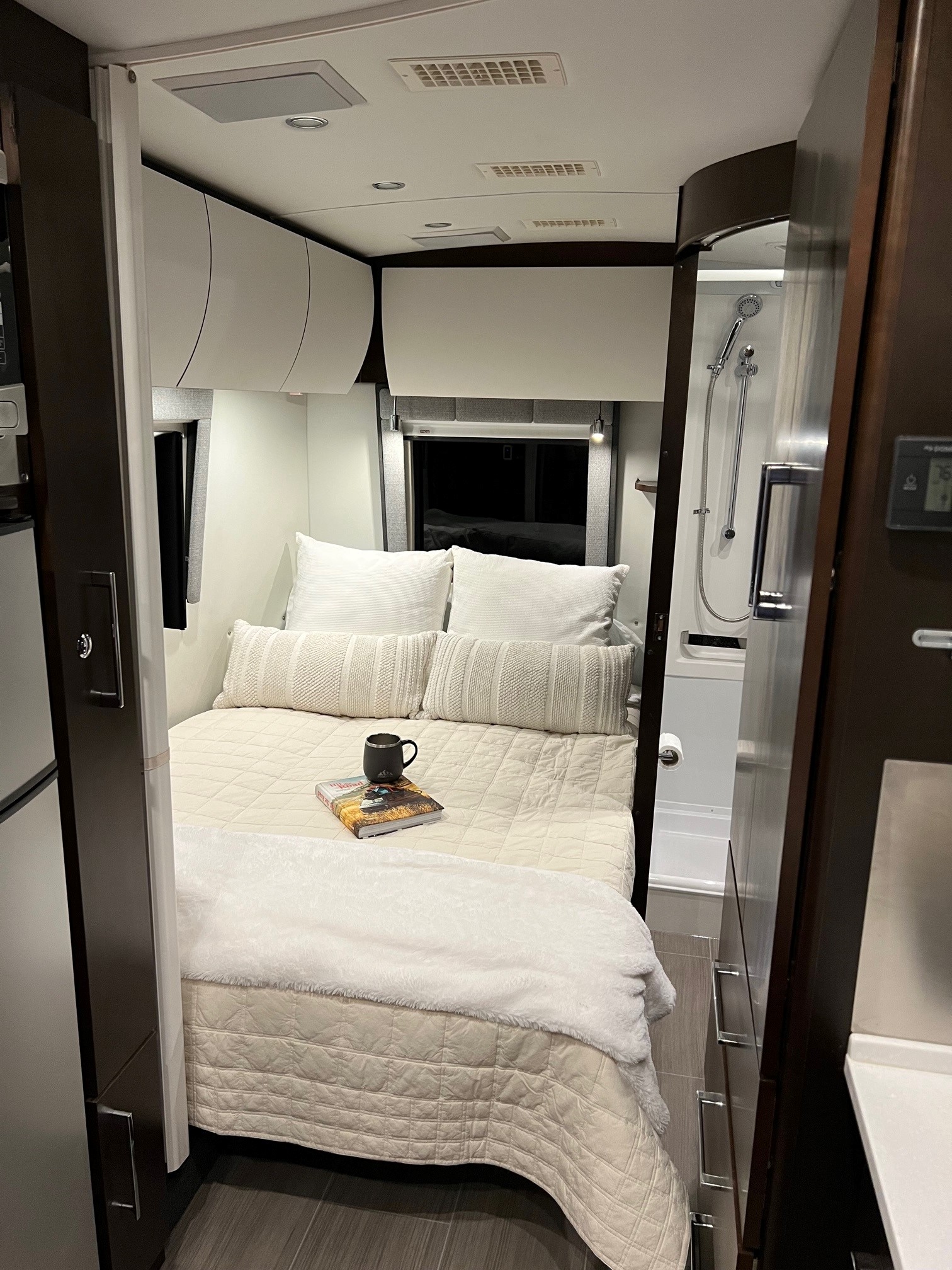 RV rental interior: a cozy bedroom with a modern bed, white cabinets, and compact shower visible on the right.. Leisure Travel Vans Serenity 2019