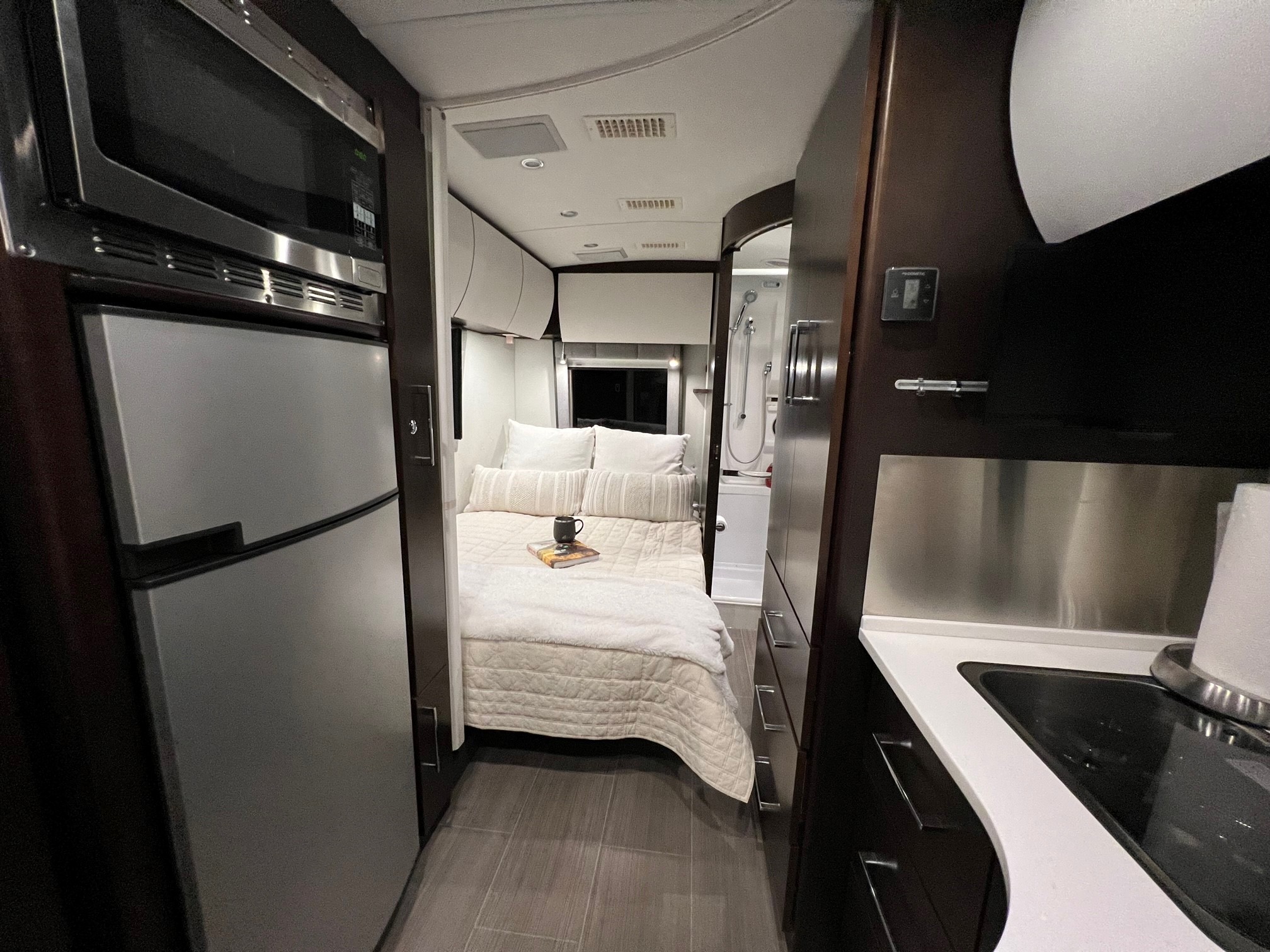 Cozy, modern RV rental interior features a compact kitchen with a sink, central bedroom, and rear bathroom with a shower.. Leisure Travel Vans Serenity 2019