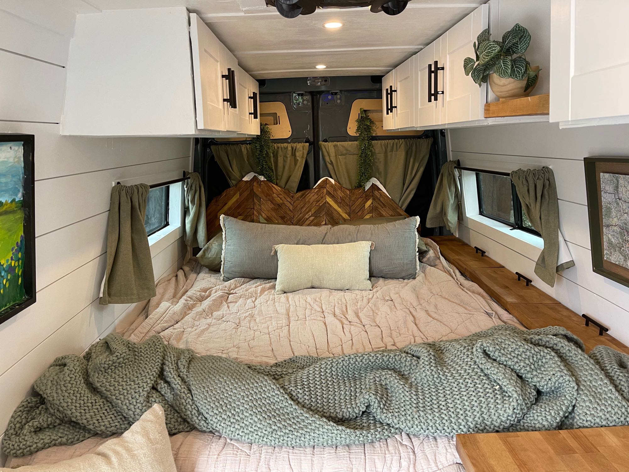 Cozy RV rental bedroom with a custom mountain headboard, comfy bedding, white cabinets, and wood accents.. Mercedes-Benz Sprinter 2021