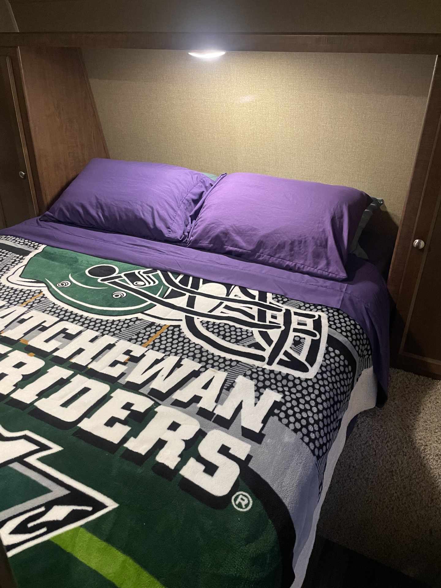 Cozy RV rental bedroom with purple bedding and a Saskatchewan Riders blanket.. Keystone Hideout 2017