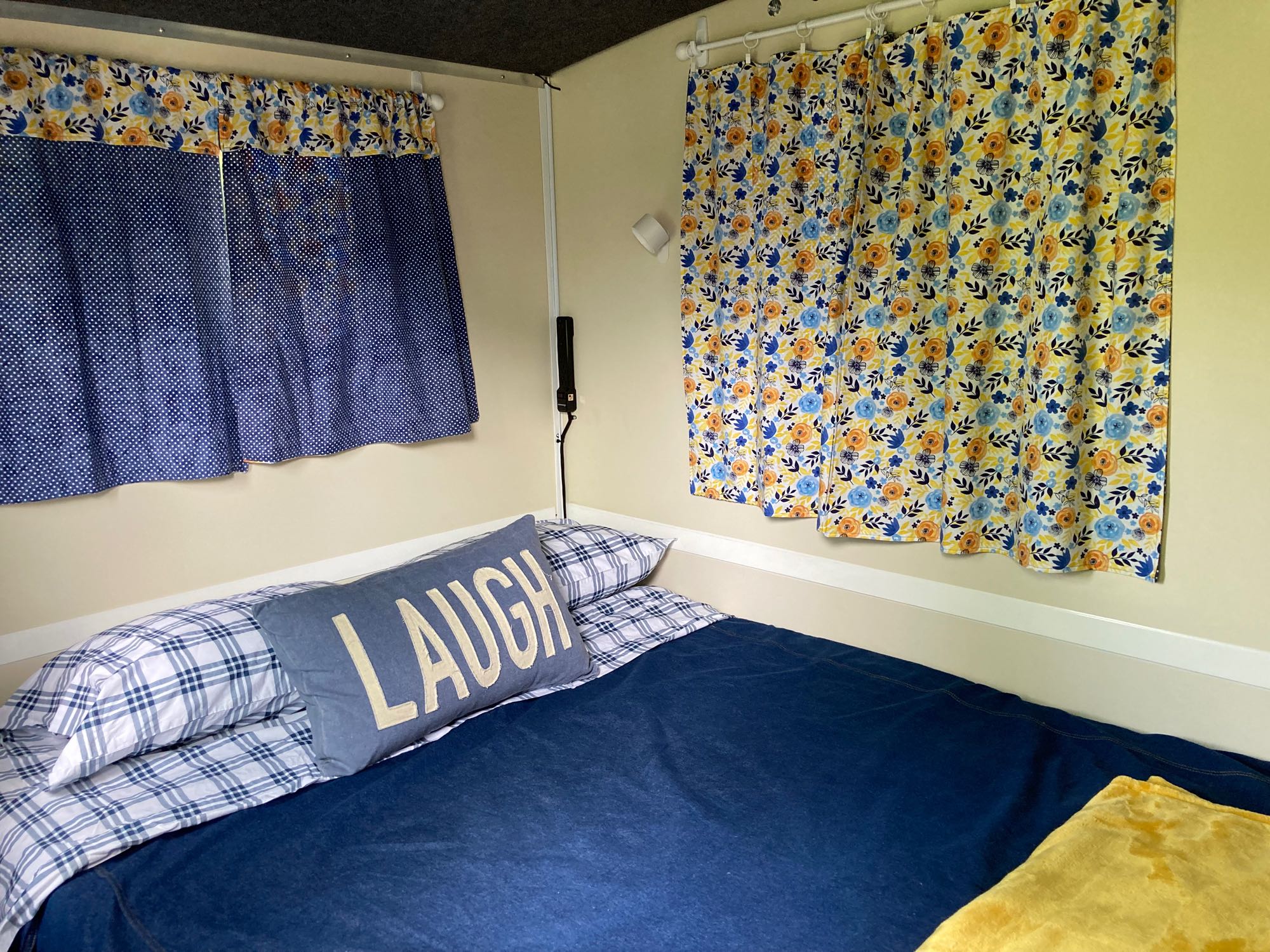 Cozy RV rental bedroom with colorful floral and polka dot curtains, a comfy bed, and a "LAUGH" pillow.. Runaway Rouser 2023