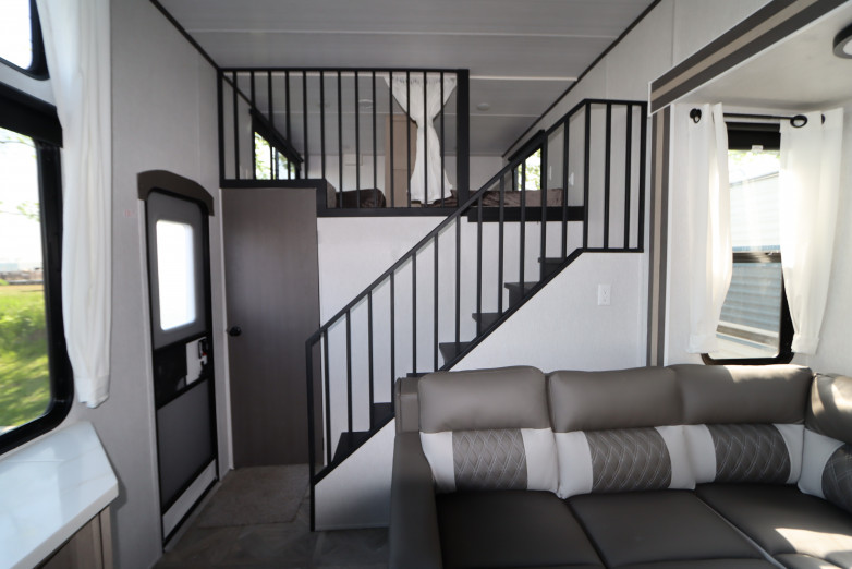 Modern RV rental interior: L-shaped sofa, staircase to a sleeping loft, and bright windows.. Forest River Salem 2023