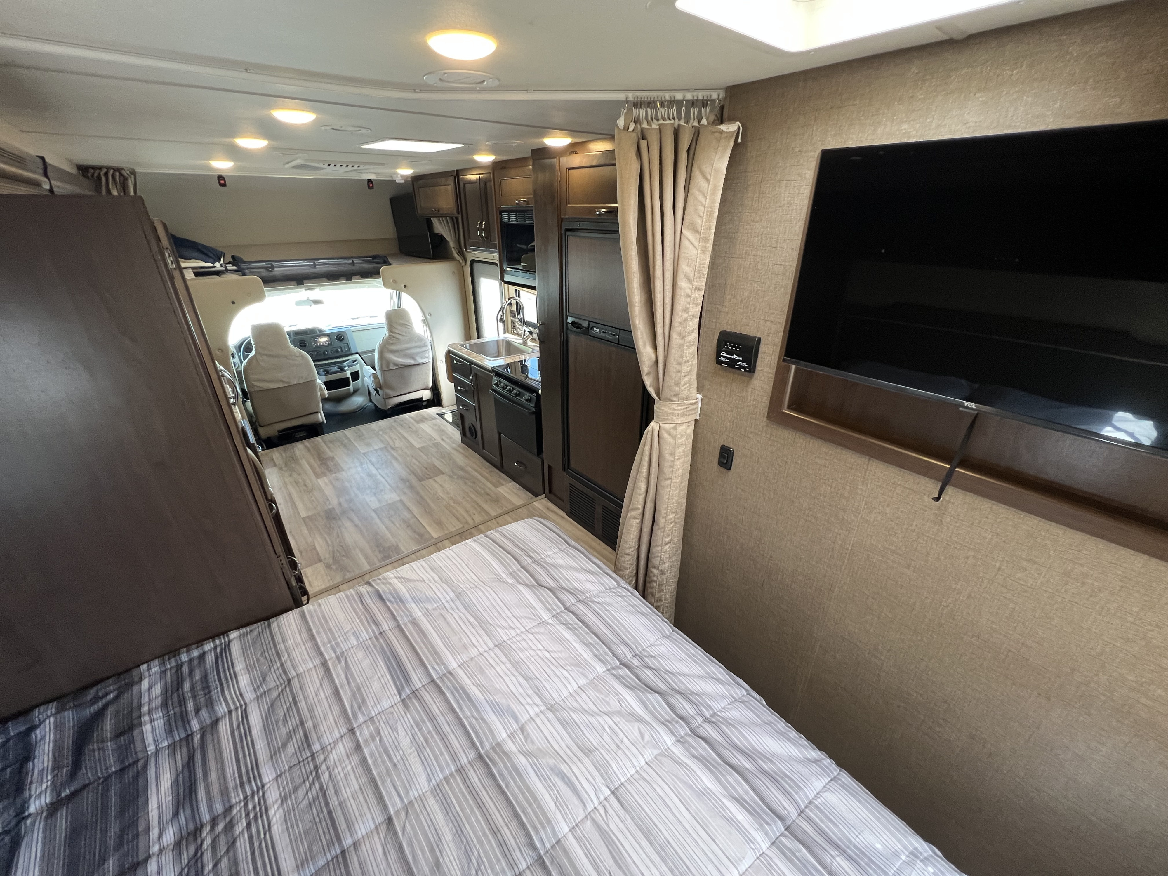 Spacious RV rental interior showing a comfortable bed, functional kitchenette, and driver's cabin. Ideal for travel.. Thor Motor Coach Freedom Elite 2018