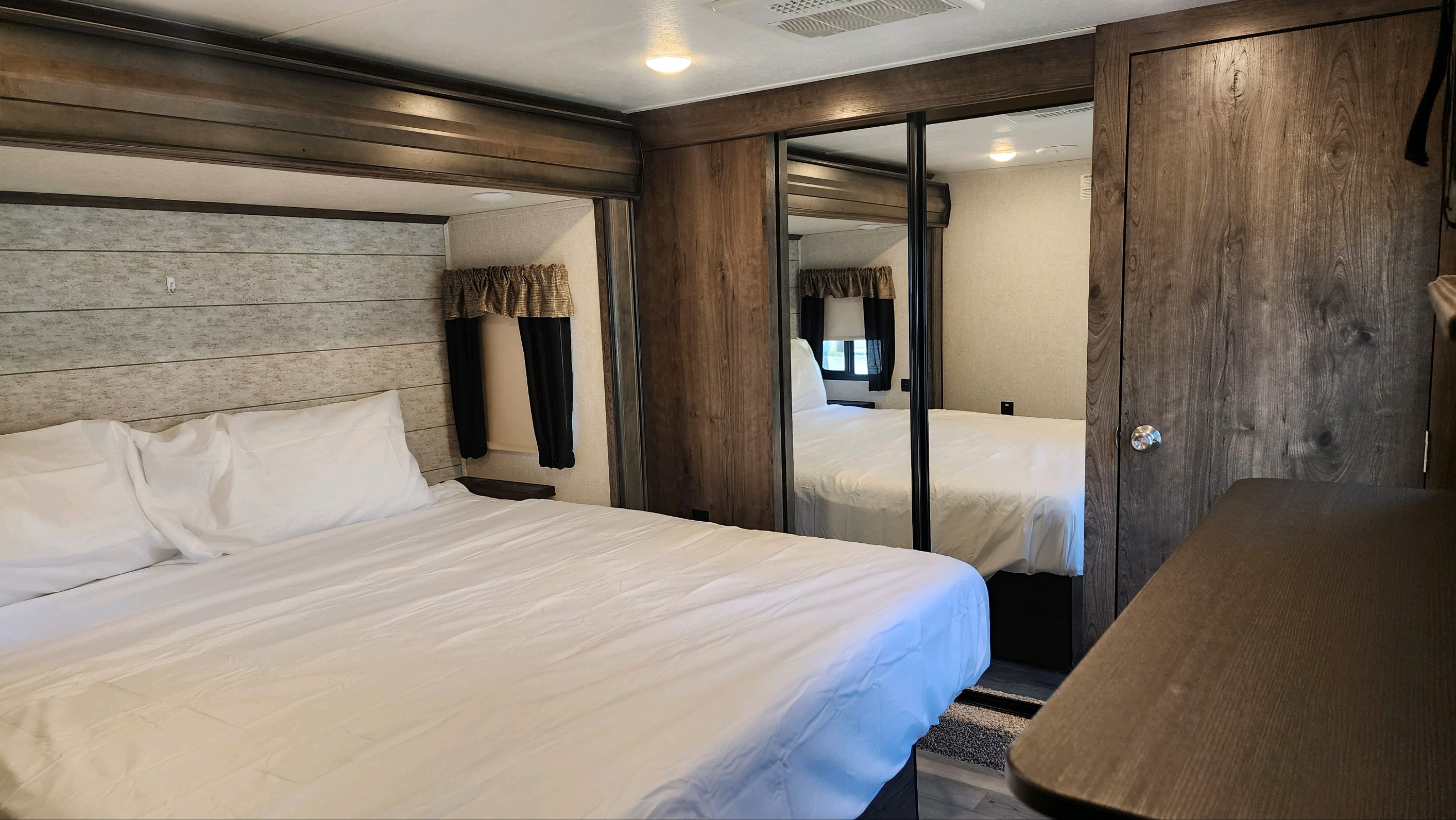Inside an RV rental: cozy bedroom with a neatly made bed, wood-planked headboard, and mirrored closet.. Keystone RV Montana High Country 2019