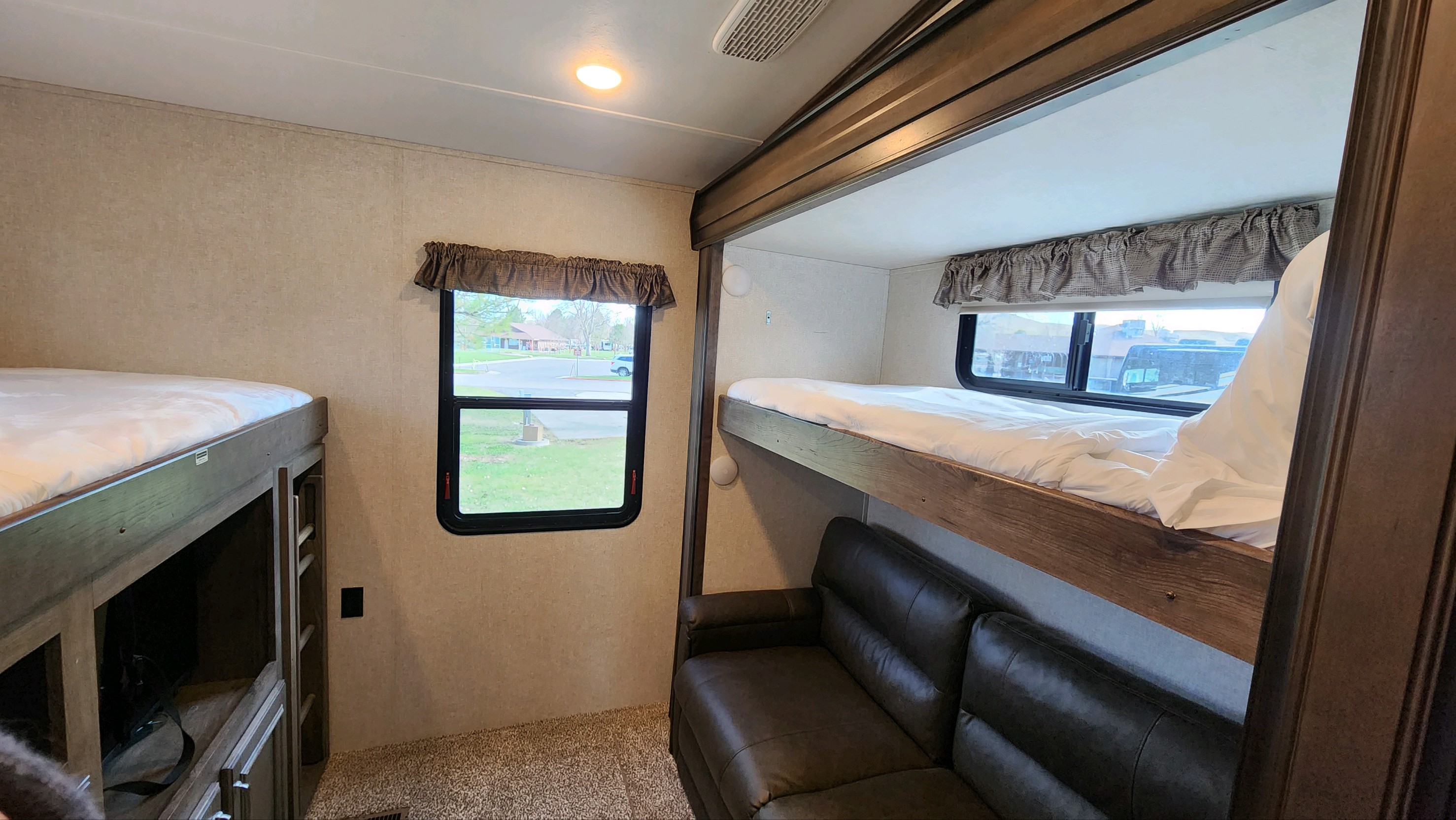 Spacious RV rental interior featuring two sets of wooden bunk beds, a comfy leather sofa, and a window view.. Keystone RV Montana High Country 2019