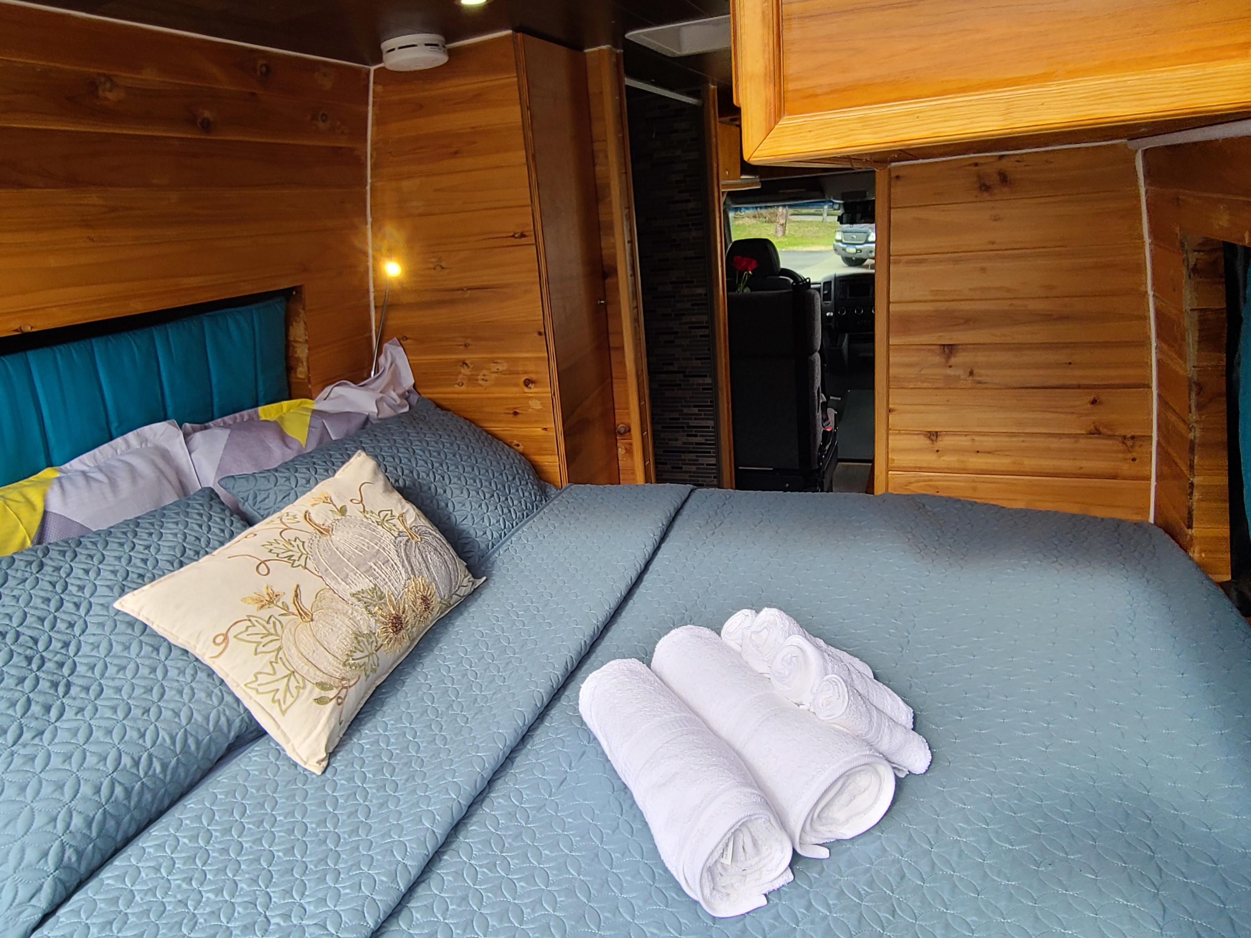 Comfortable RV rental bedroom: blue quilted bed, teal headboard, wood interior, and fresh towels. Ready for adventure!. Mercedes Sprinter 2015
