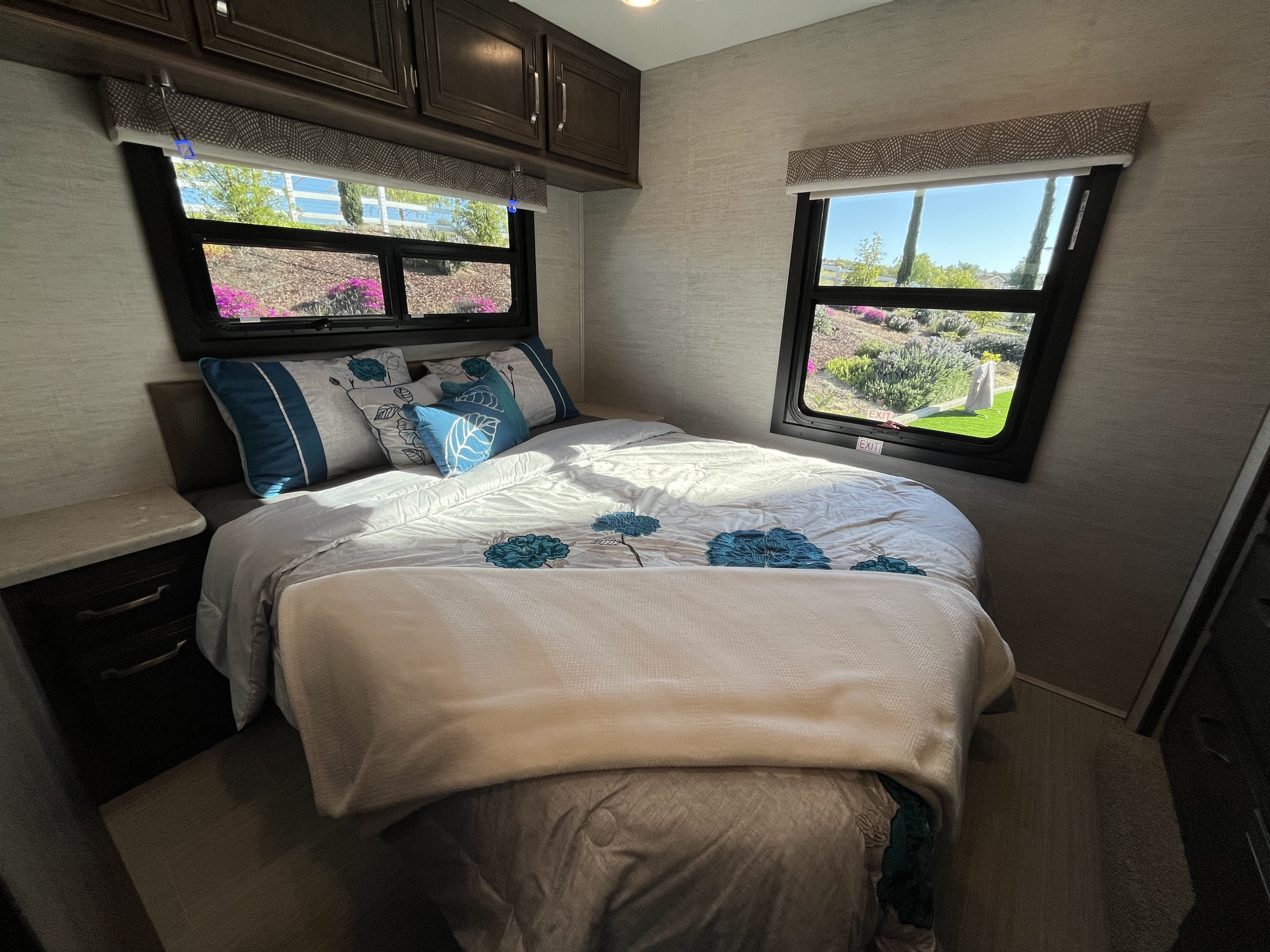Cozy RV rental bedroom featuring floral bedding, built-in storage, and bright windows with garden views.. Entegra Coach Esteem 31F 2021